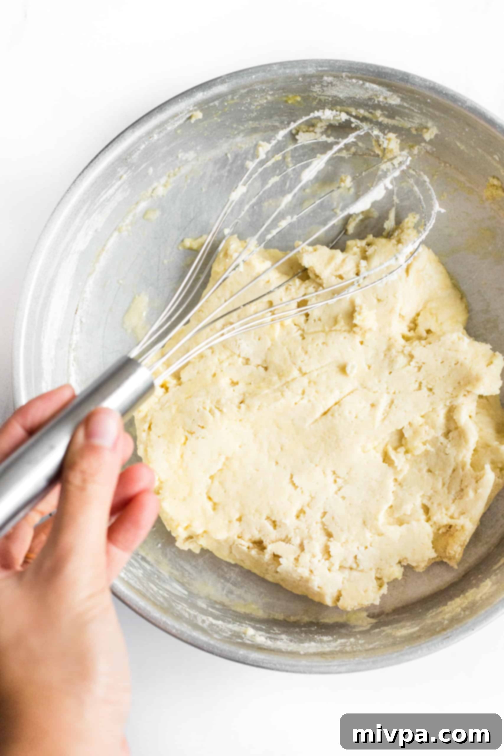 Mixing gluten-free pizza crust dough in a large metal bowl.