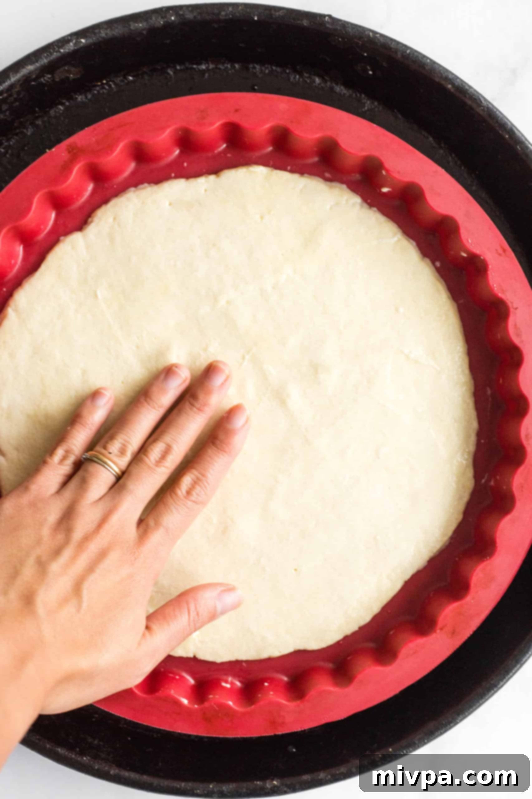 Spreading the gluten-free pizza dough on a silpat-lined pizza pan.