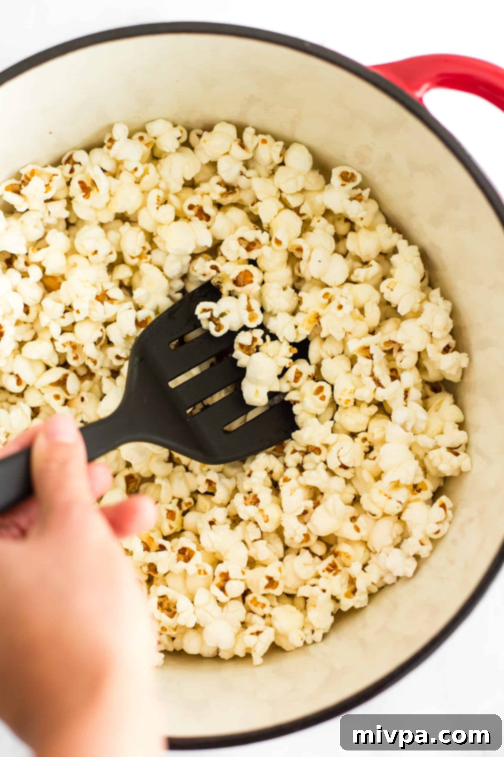 Easy Stovetop Popcorn (with Microwave option) Hand stirring freshly popped popcorn in a Dutch oven.