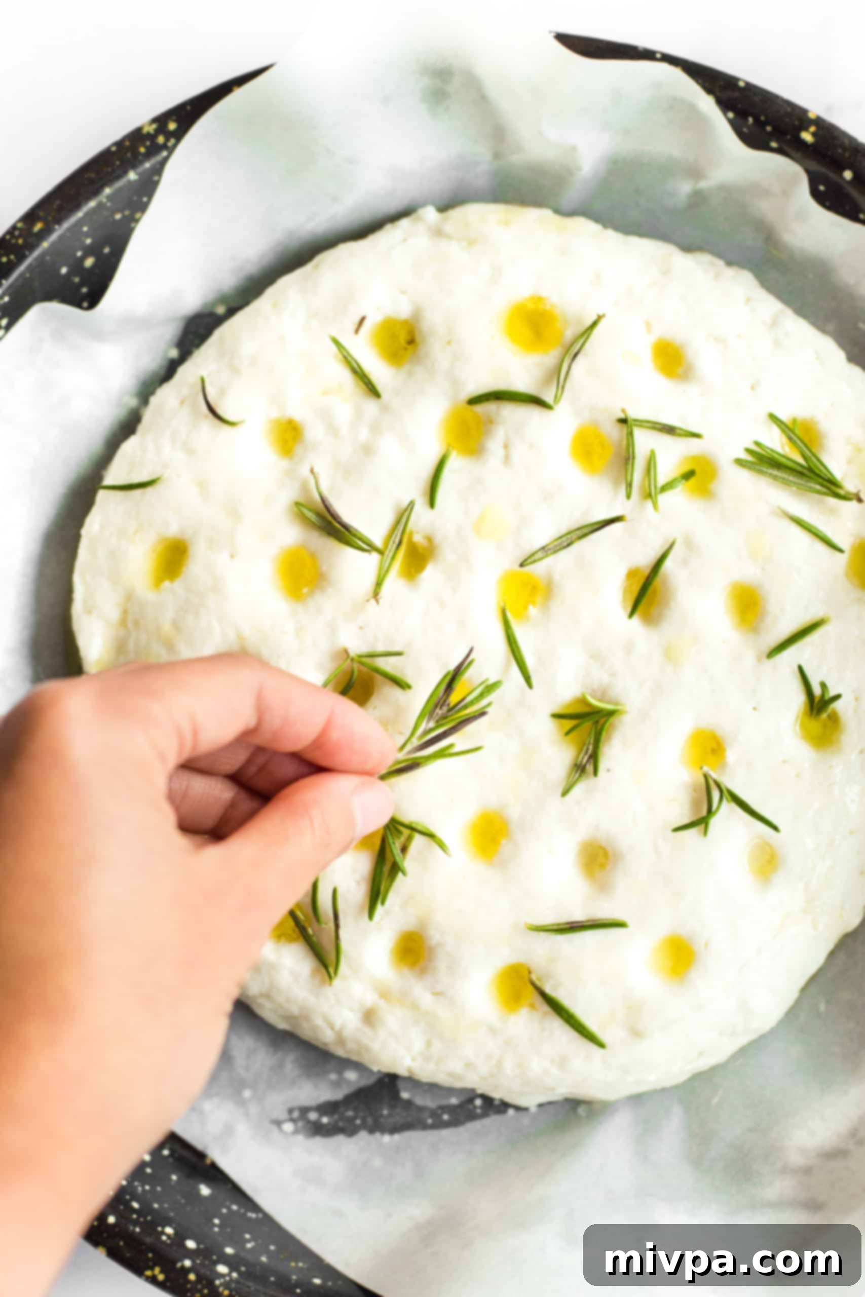 Gluten Free Focaccia Bread (Dairy-Free, Vegan) Sprinkling fresh rosemary leaves on top of gluten free focaccia dough.
