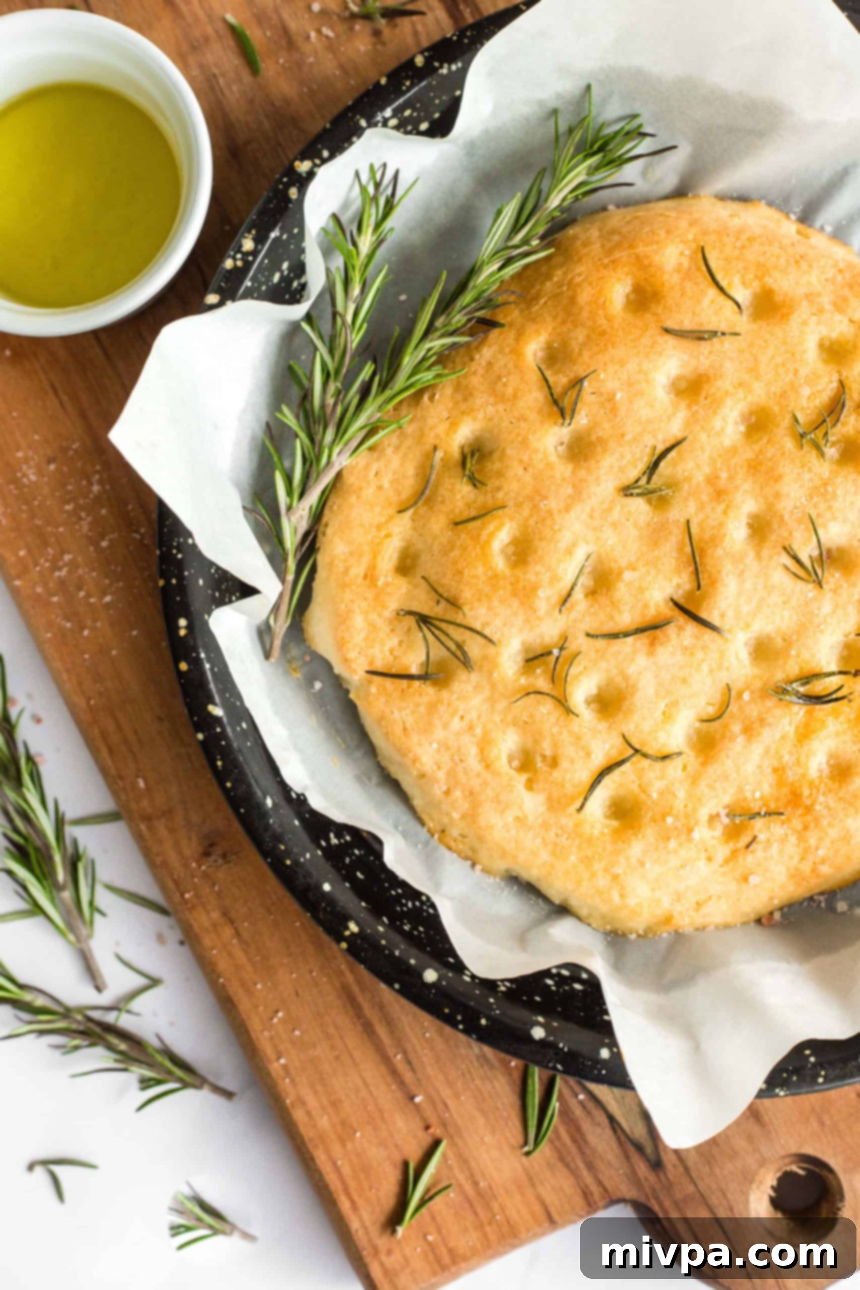 The Best Gluten-Free Focaccia Bread (Dairy-Free, Vegan) Freshly baked gluten-free rosemary focaccia bread on a parchment-lined baking sheet.