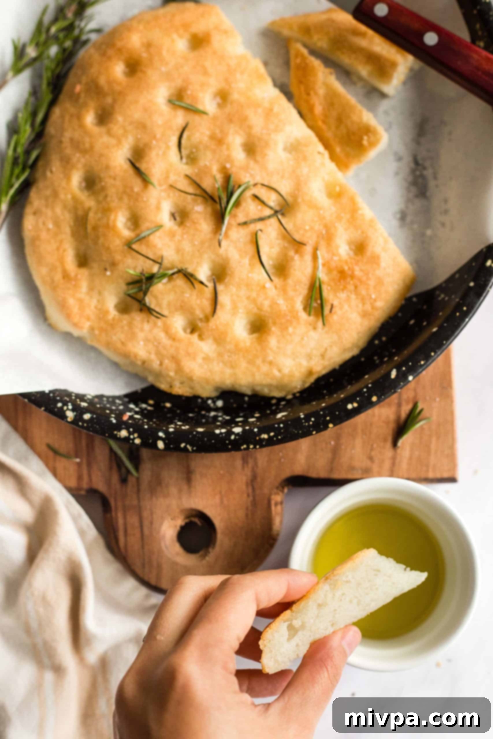 Rosemary Focaccia Bread (Gluten-Free, Vegan) Hand dipping a slice of gluten-free rosemary focaccia bread into a bowl of olive oil.