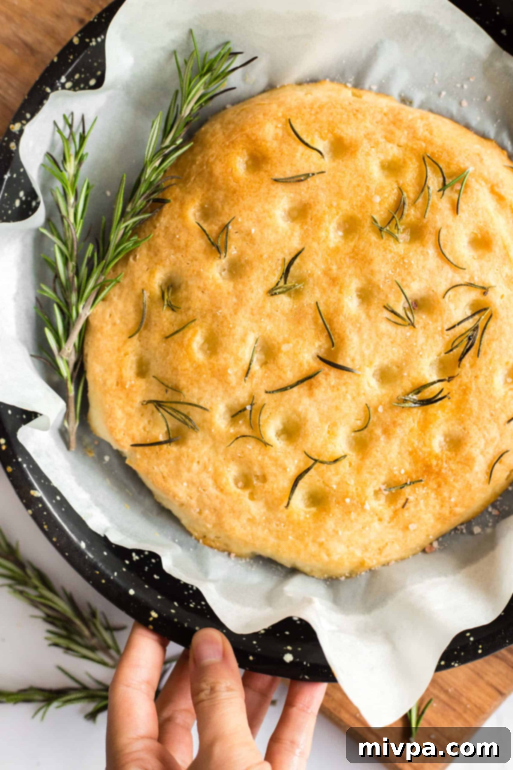 Gluten-Free Rosemary Focaccia Bread (Dairy-Free, Vegan) Hand holding a baking sheet with gluten-free focaccia bread.