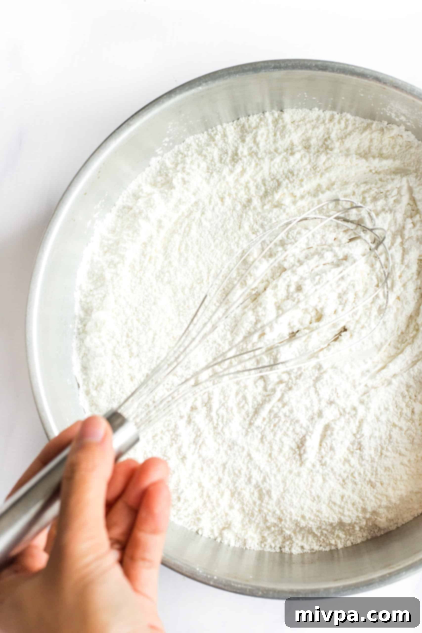 The Best Gluten-Free Focaccia Bread (Dairy-Free, Vegan) Hand whisking flour mixing in a large metal bowl.