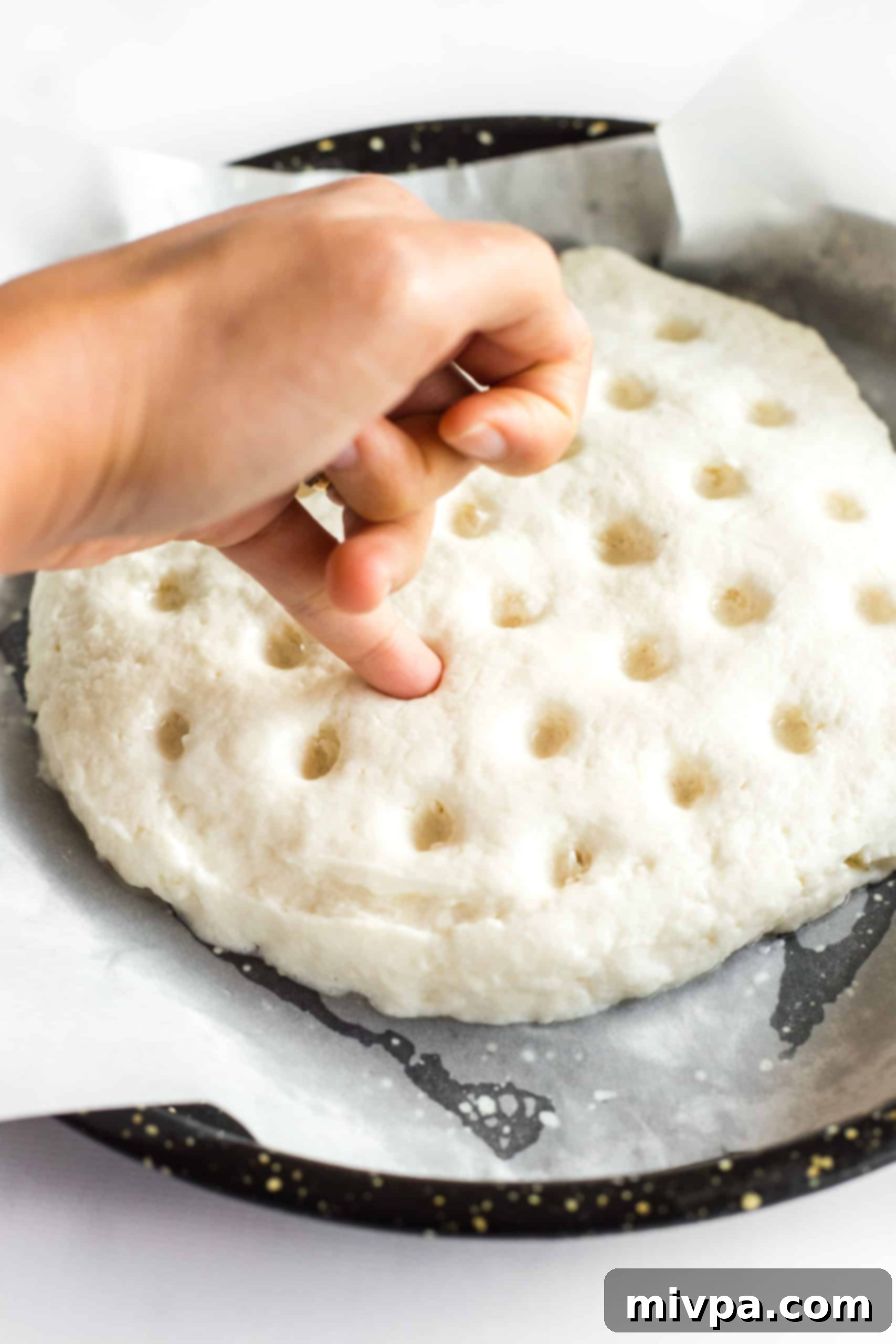 Gluten-Free Focaccia Bread Recipe (Dairy-Free, Vegan) Pinky finger poking holes into risen gluten-free focaccia bread dough to create characteristic dimples.