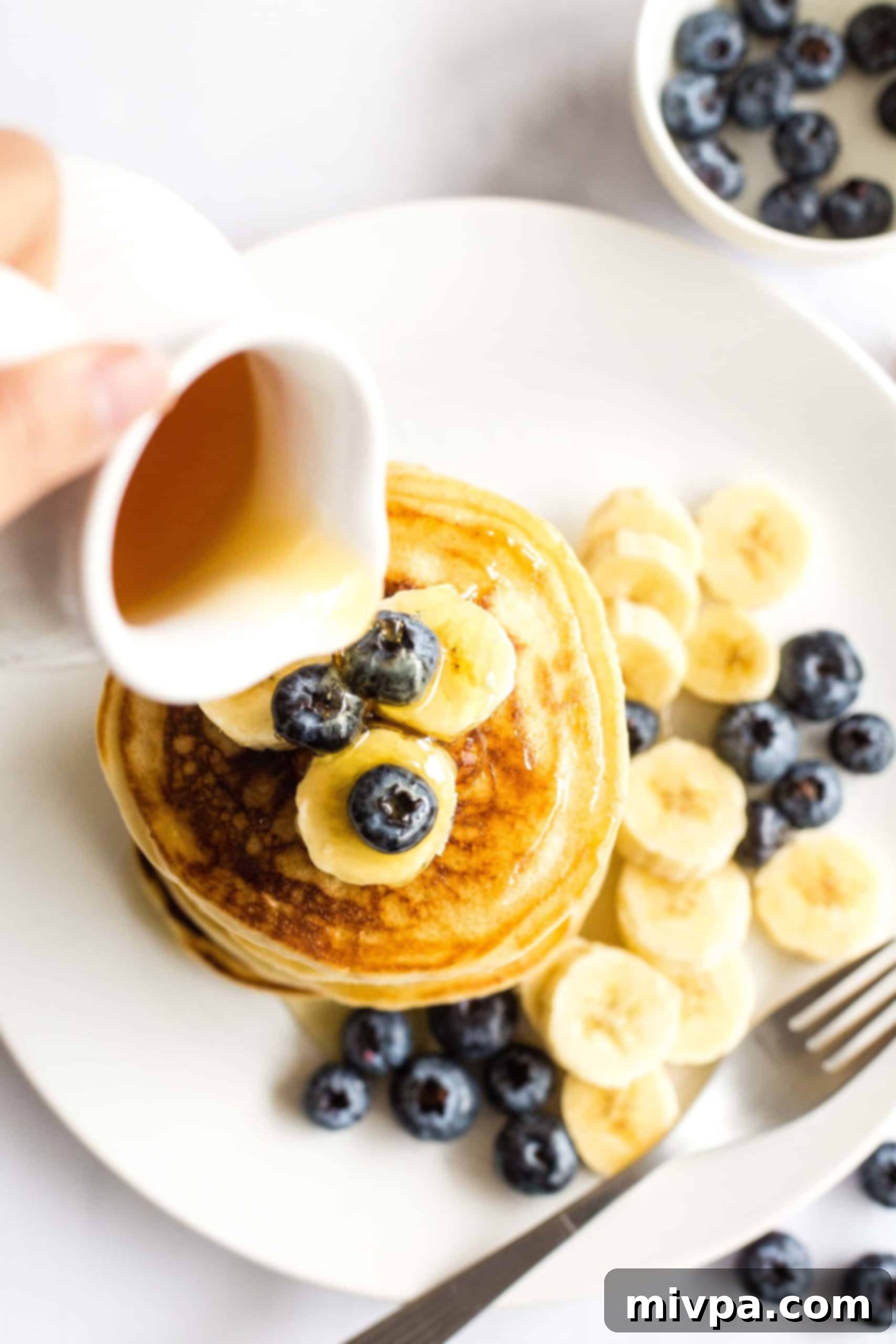 Fluffy Gluten-Free Pancakes (Dairy-Free) A hand pouring maple syrup onto a stack of gluten-free pancakes, creating an inviting visual.