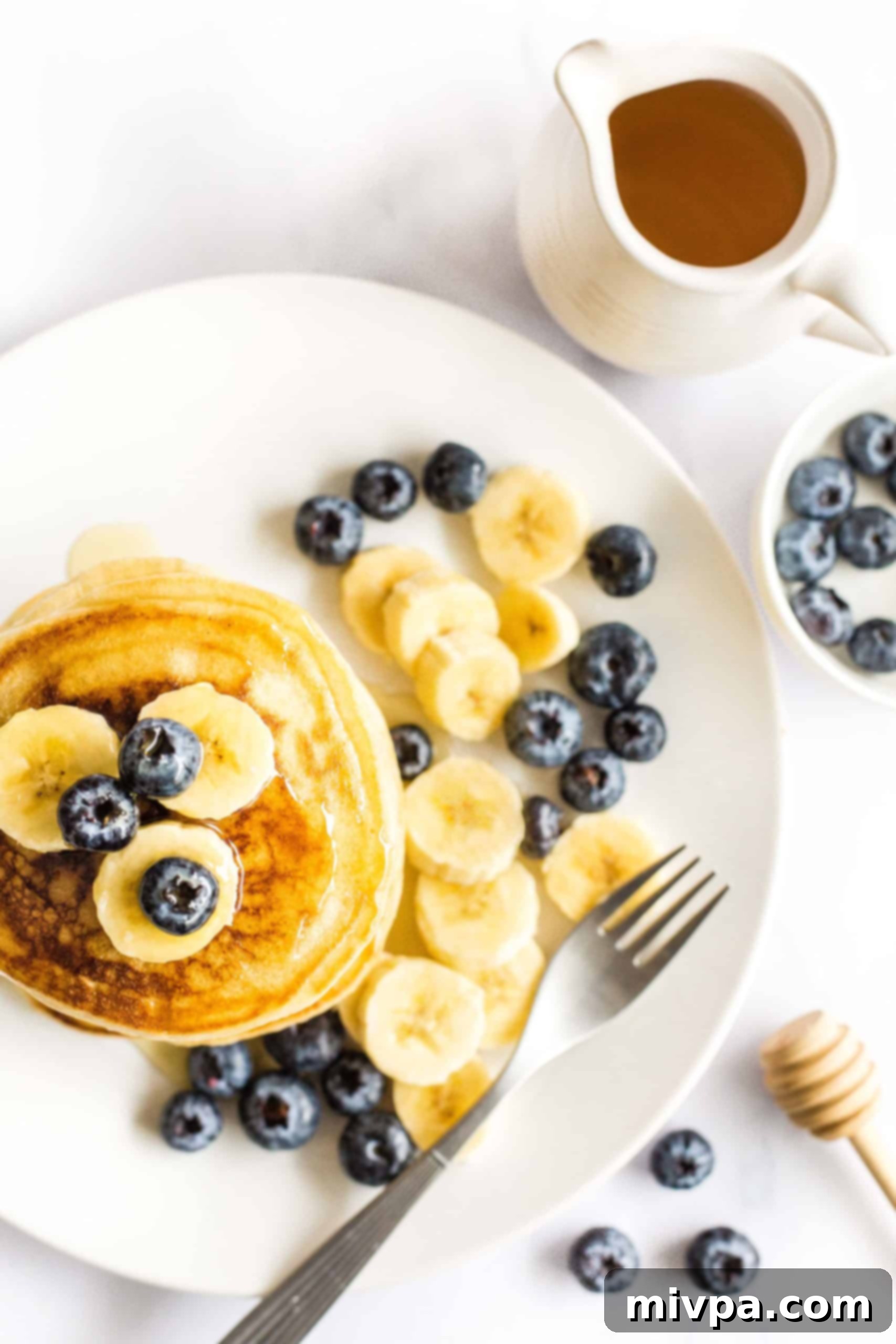 Fluffy Gluten-Free Pancakes (Dairy-Free) Gluten-free pancakes on a plate with blueberries and sliced bananas, drizzled in maple syrup for a perfect breakfast.
