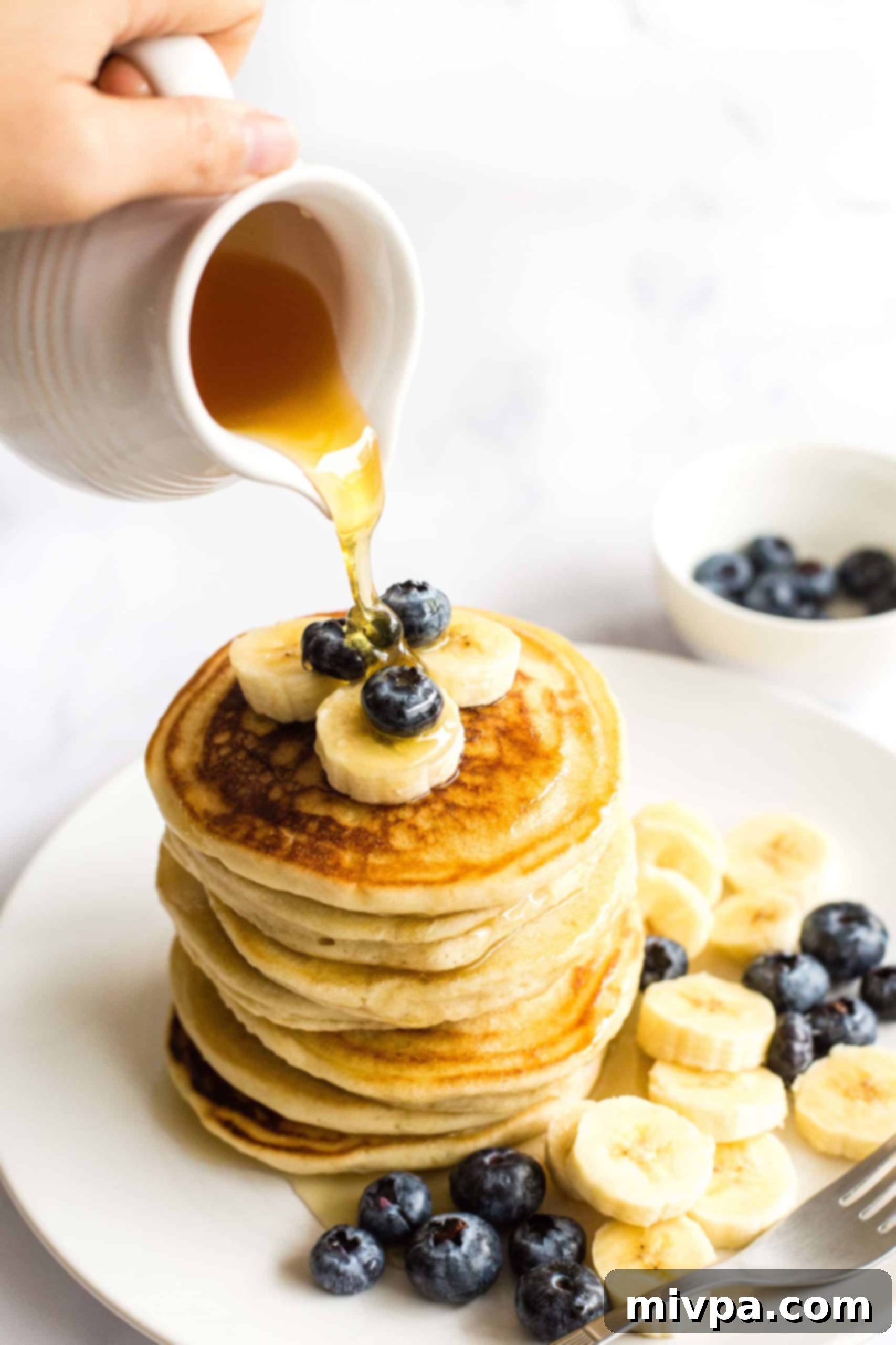Fluffy Gluten-Free Pancakes (Dairy-Free) A hand pouring maple syrup generously over a stack of fluffy gluten-free pancakes, highlighting their perfect texture.