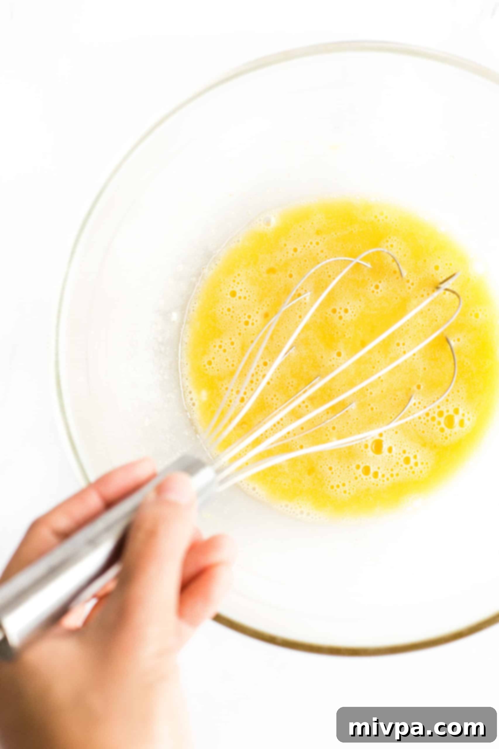 Fluffy Gluten-Free Pancakes (Dairy-Free) Eggs, sugar, oil, and vanilla whisked in a large mixing bowl, showing a pale yellow, airy mixture.