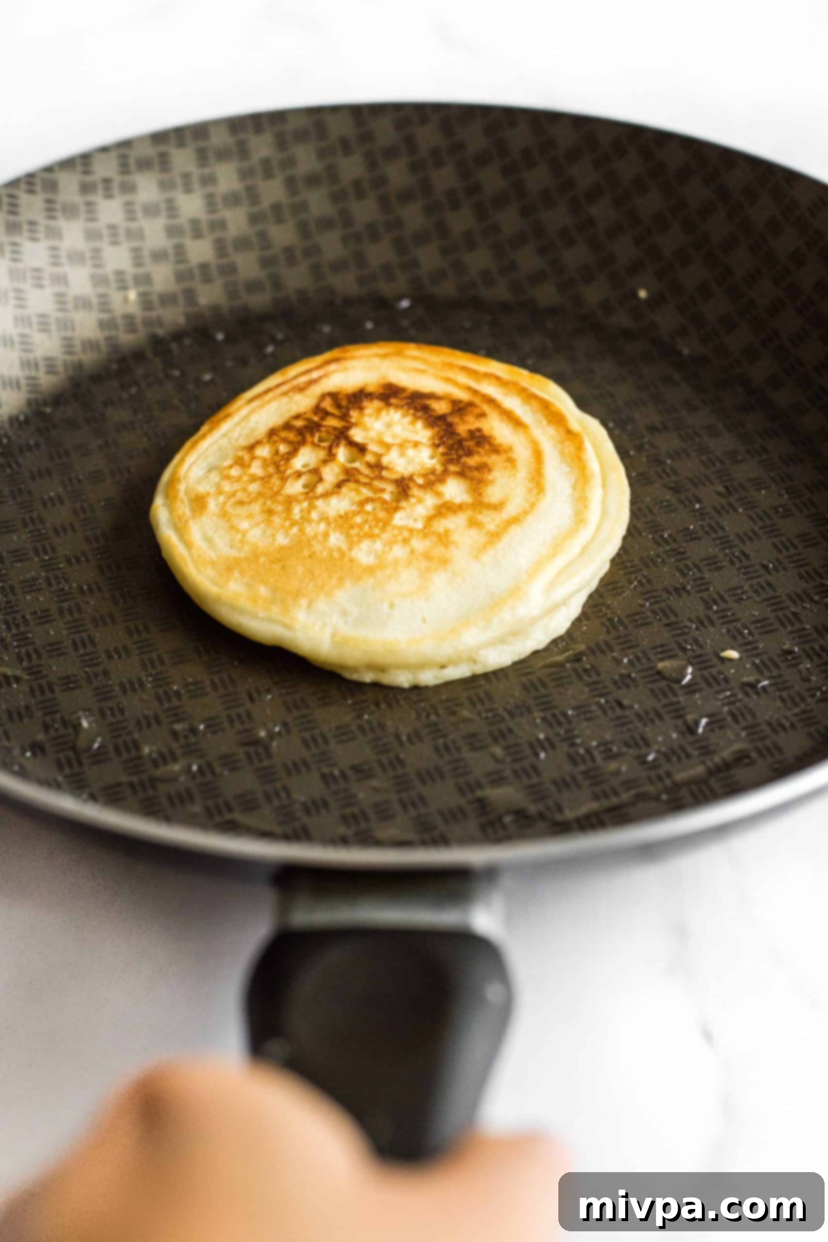 Fluffy Gluten-Free Pancakes (Dairy-Free) Cooking a pancake in a non-stick skillet, showing bubbles forming on the surface as it cooks.