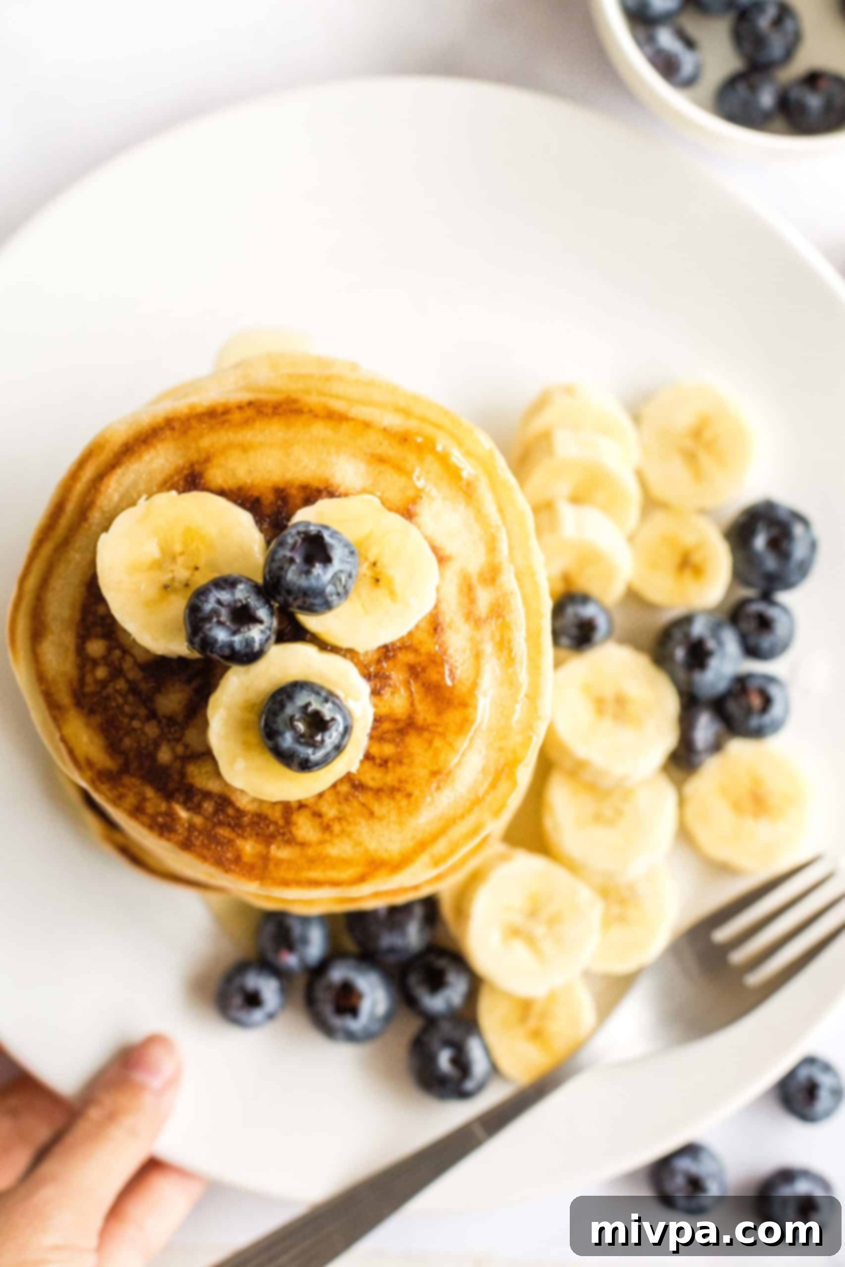 Fluffy Gluten-Free Pancakes (Dairy-Free) Gluten-free pancakes topped with fresh blueberries on a white plate, ready for serving.