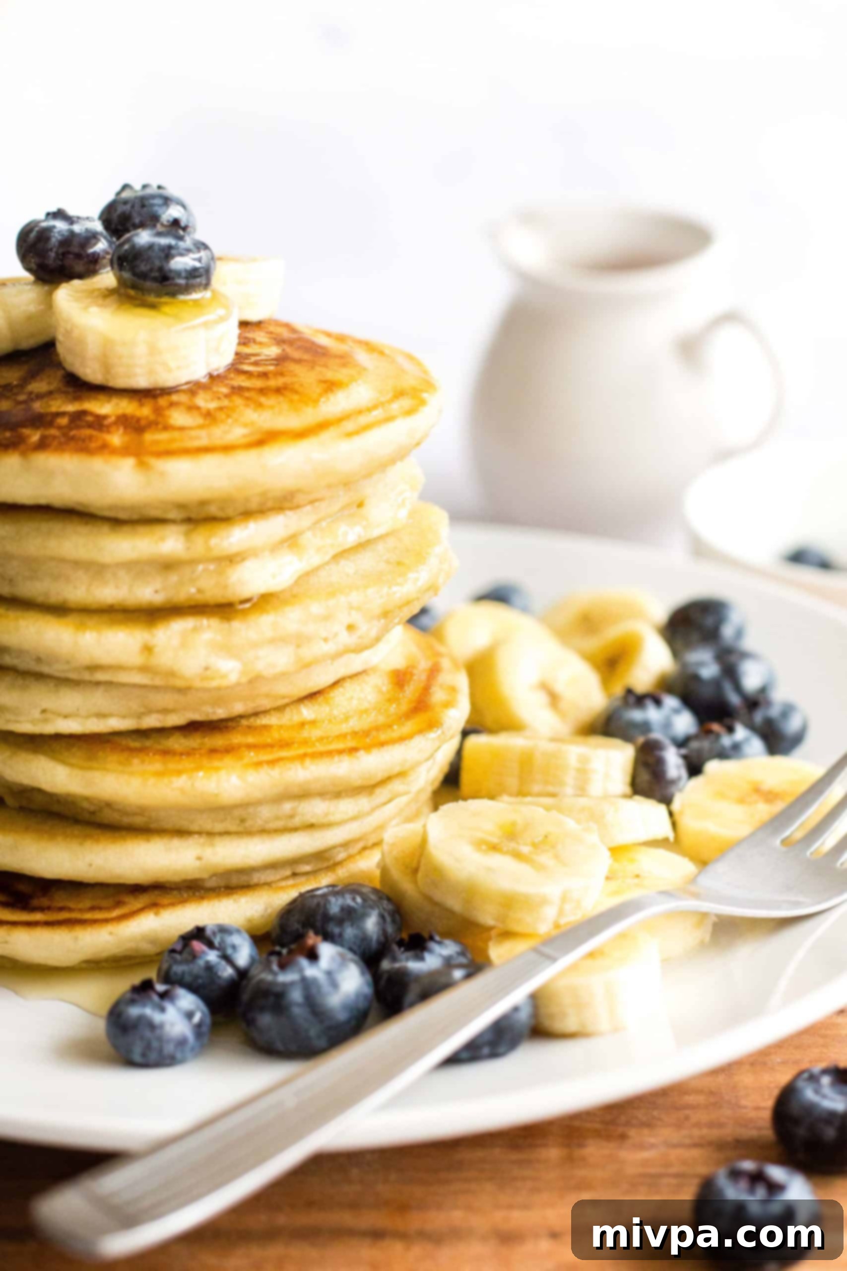 Fluffy Gluten-Free Pancakes (Dairy-Free) A tall stack of fluffy gluten-free pancakes topped with mixed fresh fruit and drizzled in maple syrup, looking inviting.
