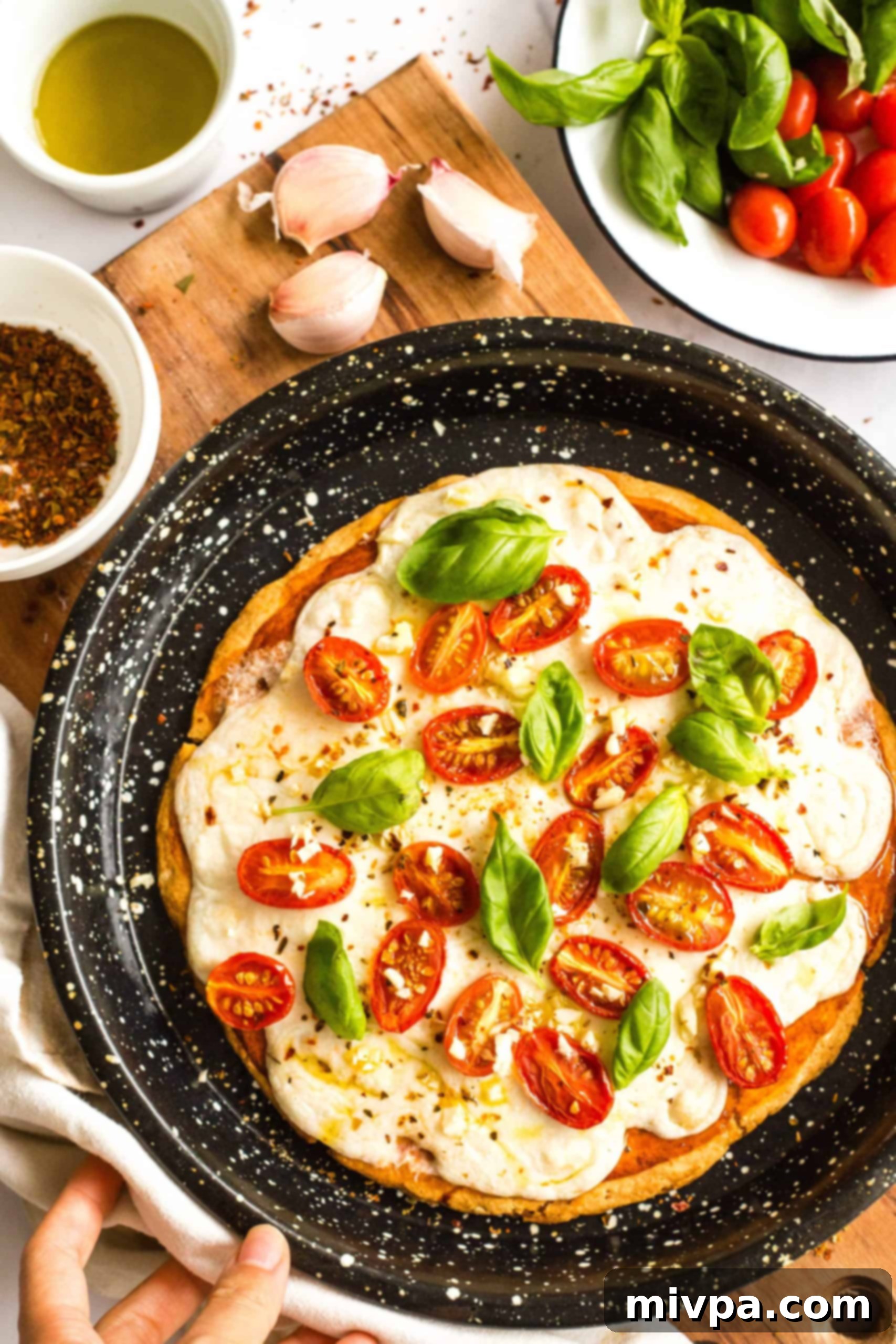 Easy Caprese Pizza (Gluten-Free, Vegan) Hand holding a pizza pan with freshly baked gluten-free caprese pizza.