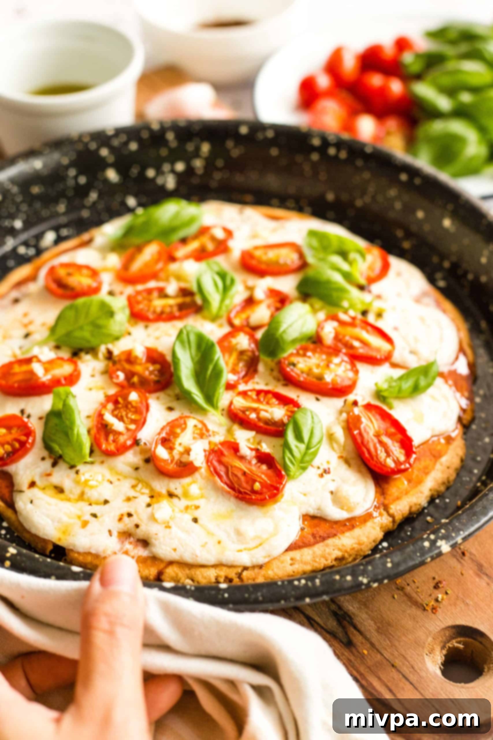 Easy Caprese Pizza (Gluten-Free, Vegan) Hand holding a pizza pan with a freshly baked gluten-free caprese pizza.