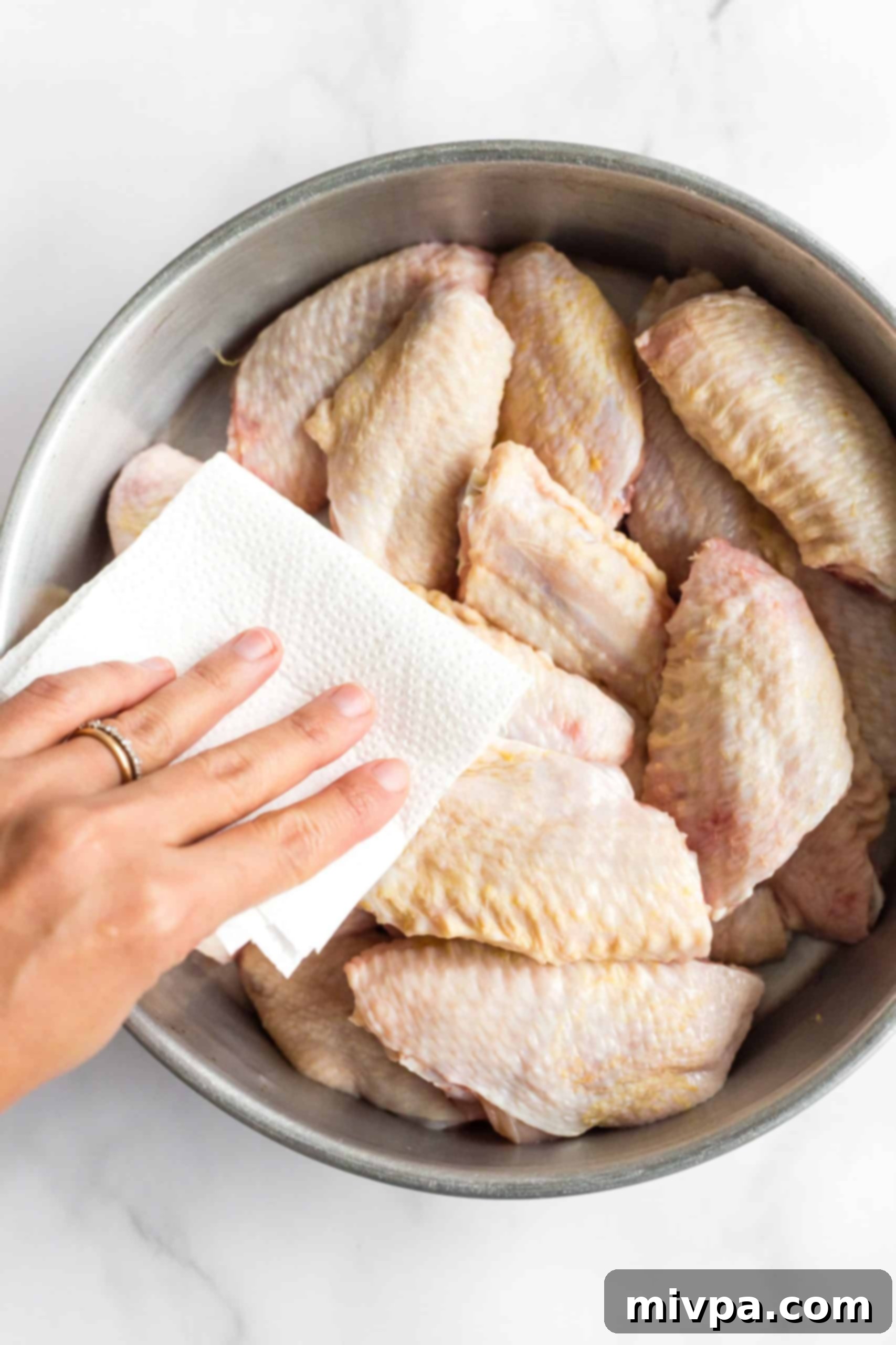A hand patting the chicken wings dry with a paper towel.