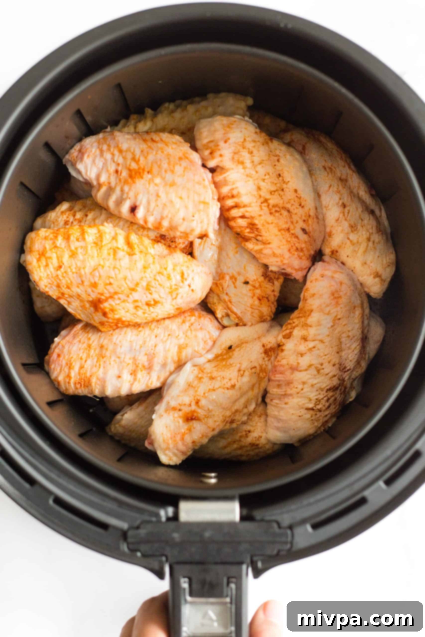 Seasoned chicken wings inside an air fryer basket ready to be cooked. 