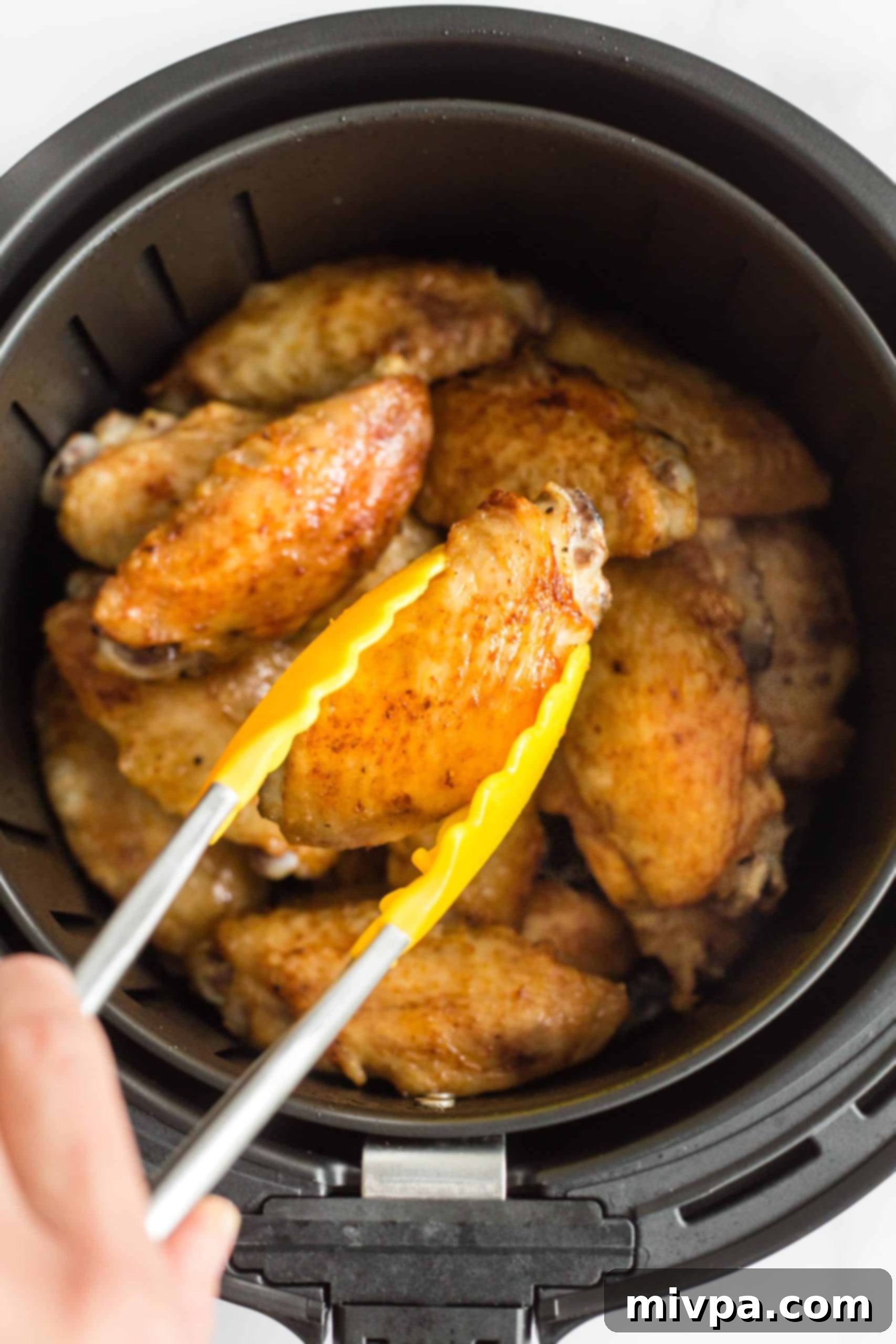 Picking up a crispy chicken wing from the air fryer basket.