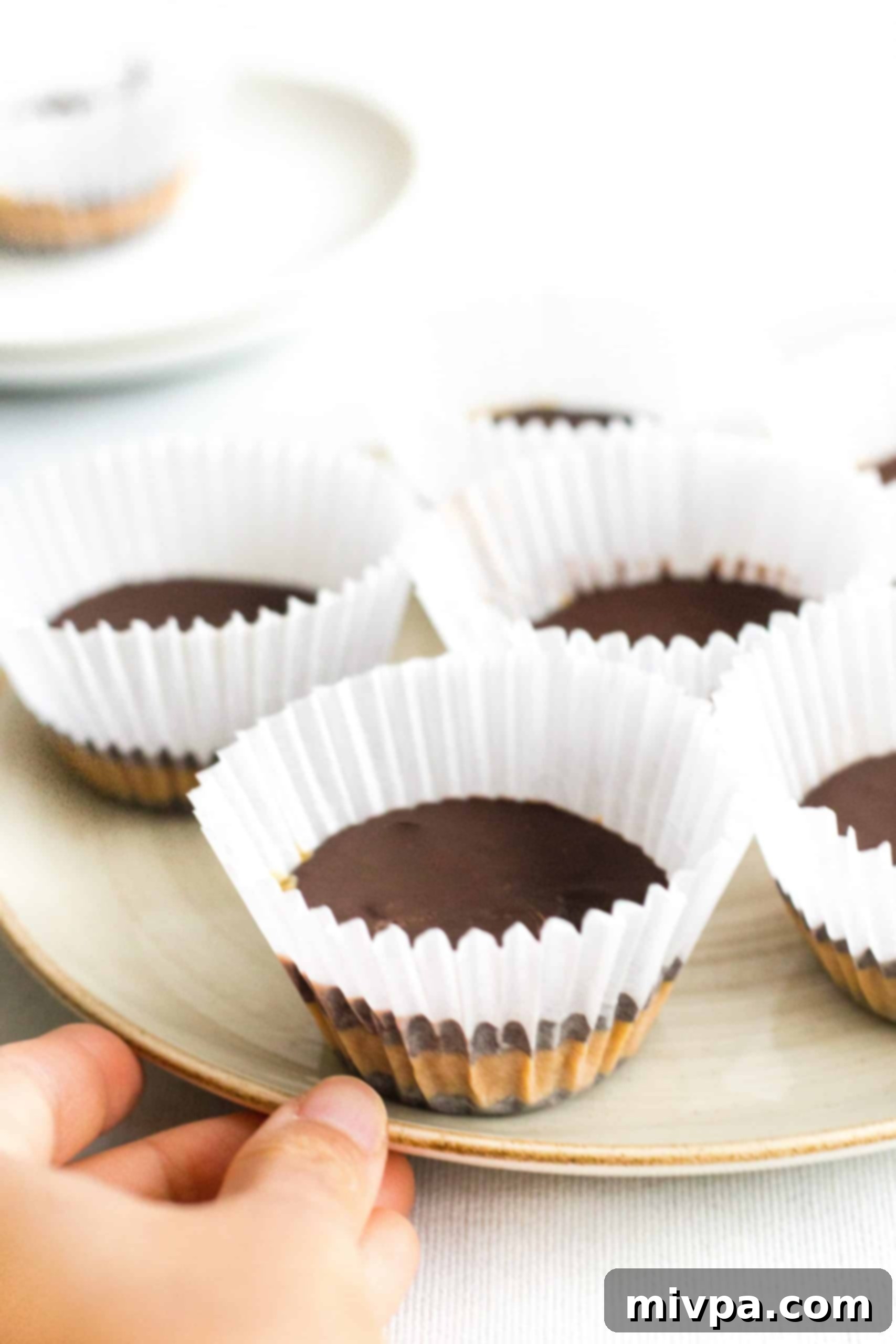 Healthy Peanut Butter Cups (Gluten-Free, Vegan) Hand holding a plate of healthy peanut butter cups in paper liners.