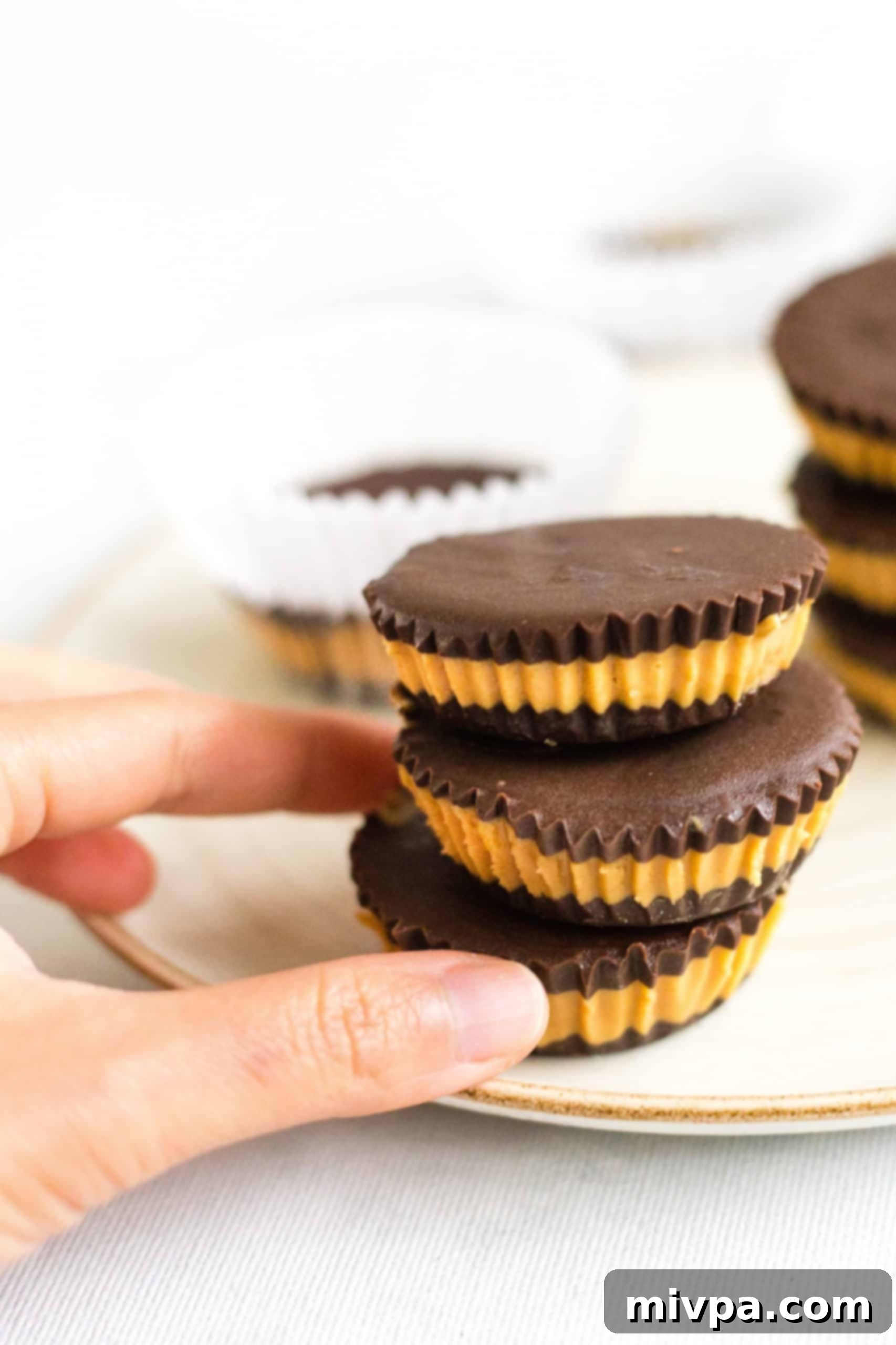 Homemade Peanut Butter Cups (Gluten-Free, Vegan) Hand reaching for a stack of chocolate peanut butter cups on a plate.