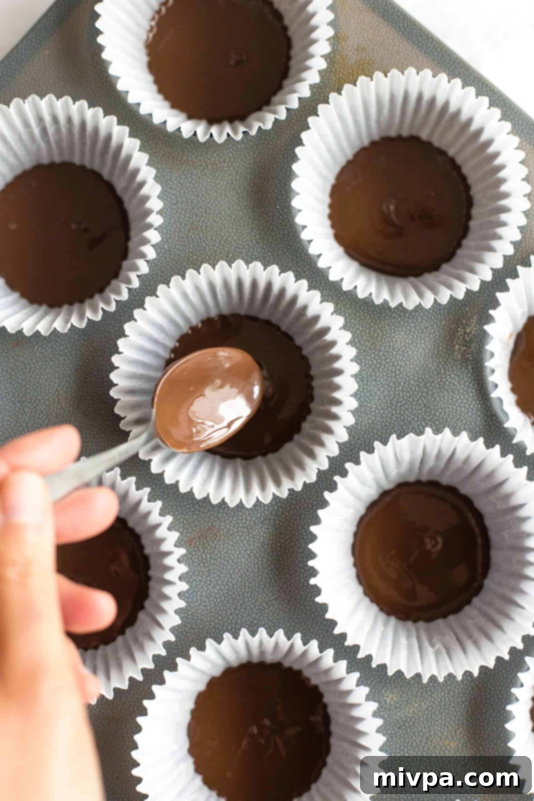 Healthy Peanut Butter Cups (Gluten-Free, Vegan) Distributing melted chocolate between paper muffin liners.