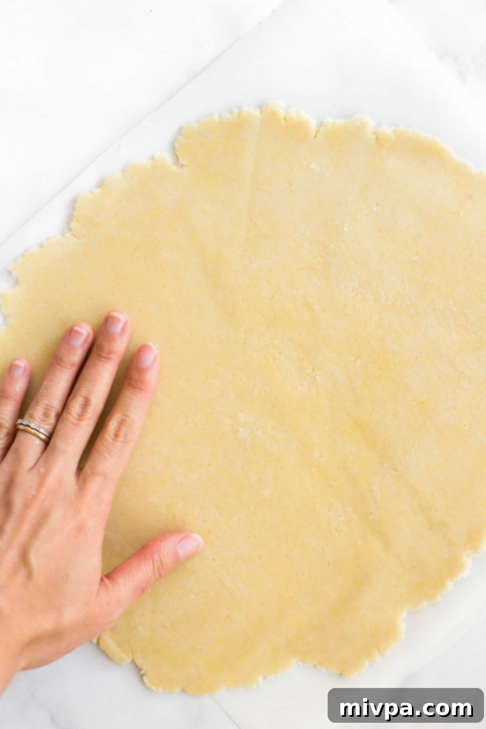 Easy Pecan Pie Recipe (Gluten-Free, Dairy-Free) Hand pressing out pie crust dough on parchment paper.