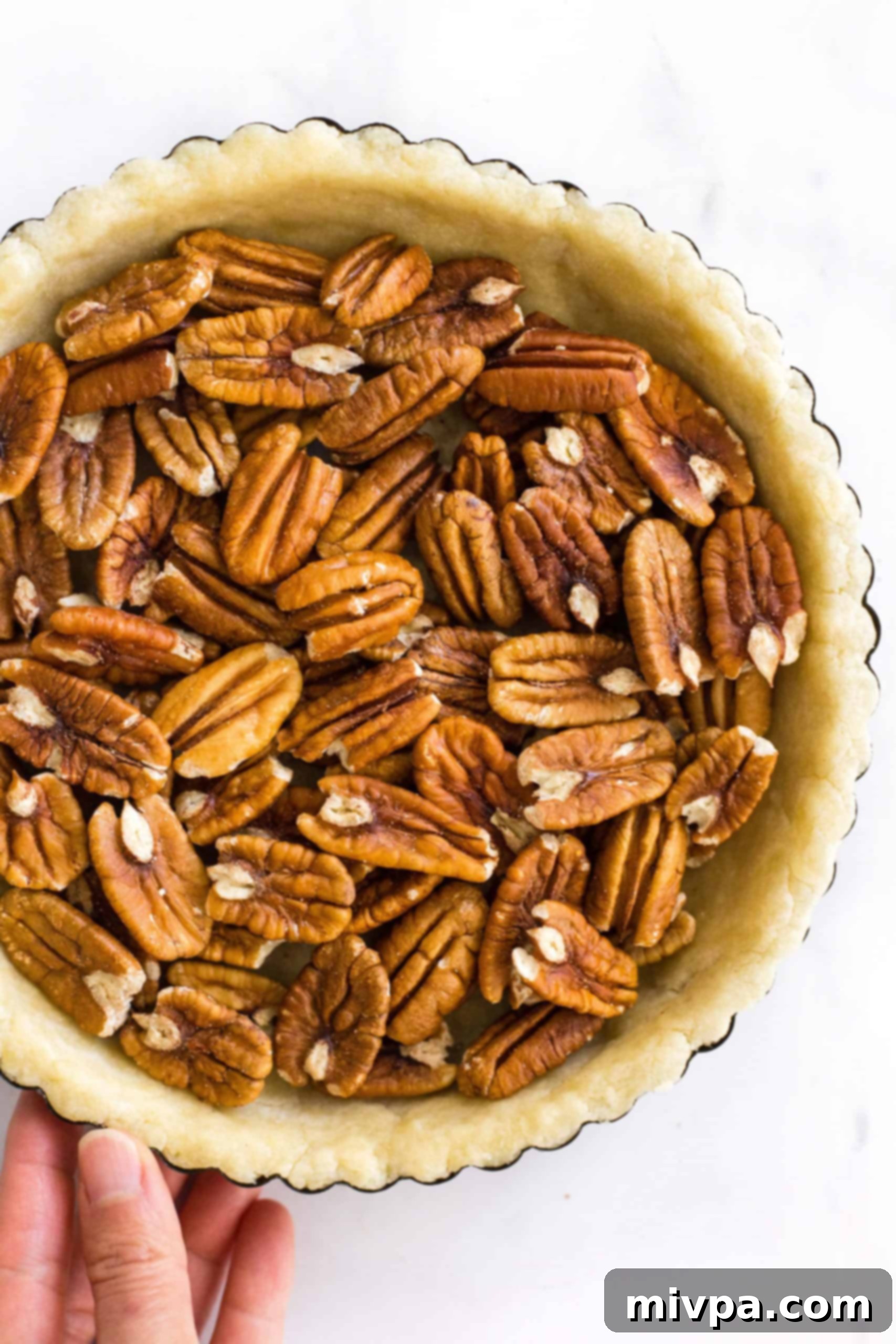 Easy Pecan Pie Recipe (Gluten-Free, Dairy-Free) Hand holding a pie tin with unbaked pie crust filled with pecans.