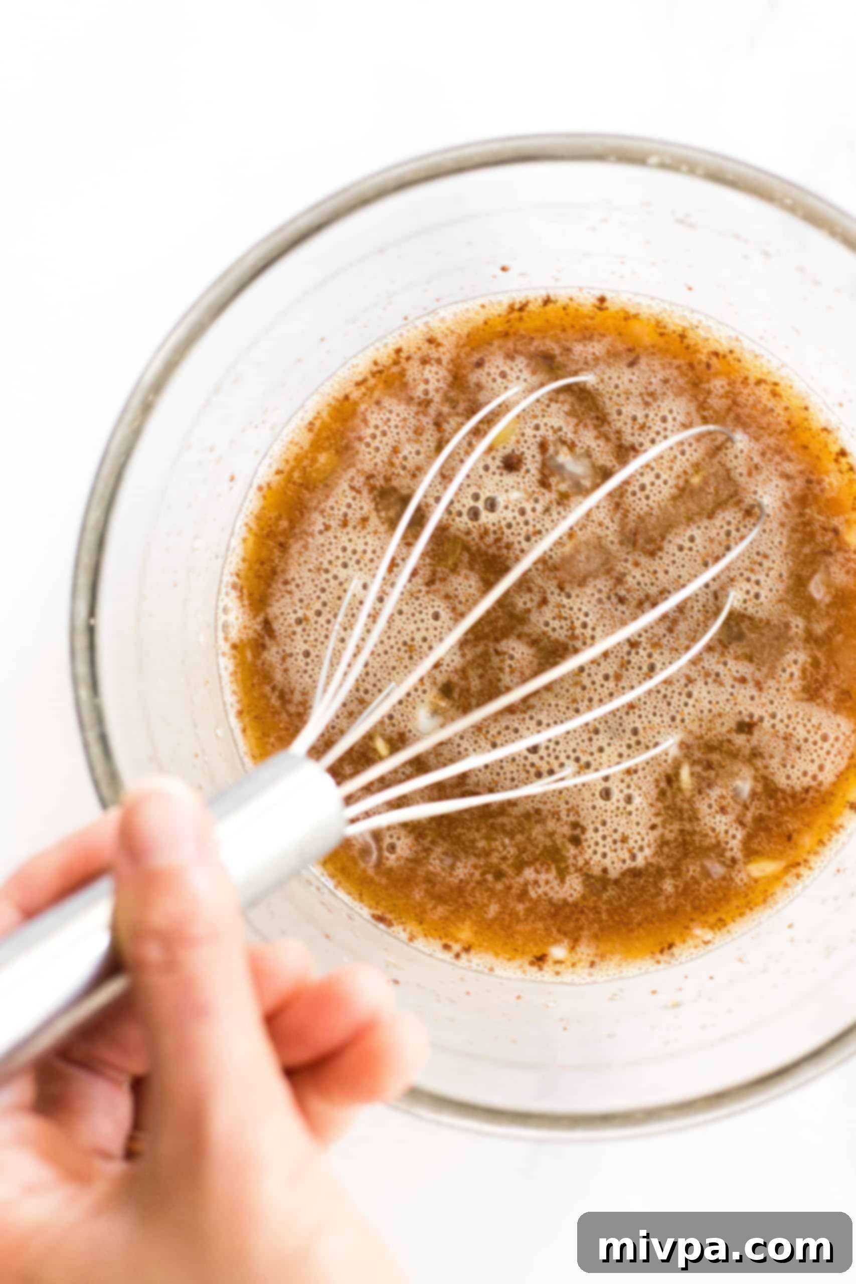 Easy Pecan Pie Recipe (Gluten-Free, Dairy-Free) Whisking a brown liquid mixture in a glass mixing bowl.