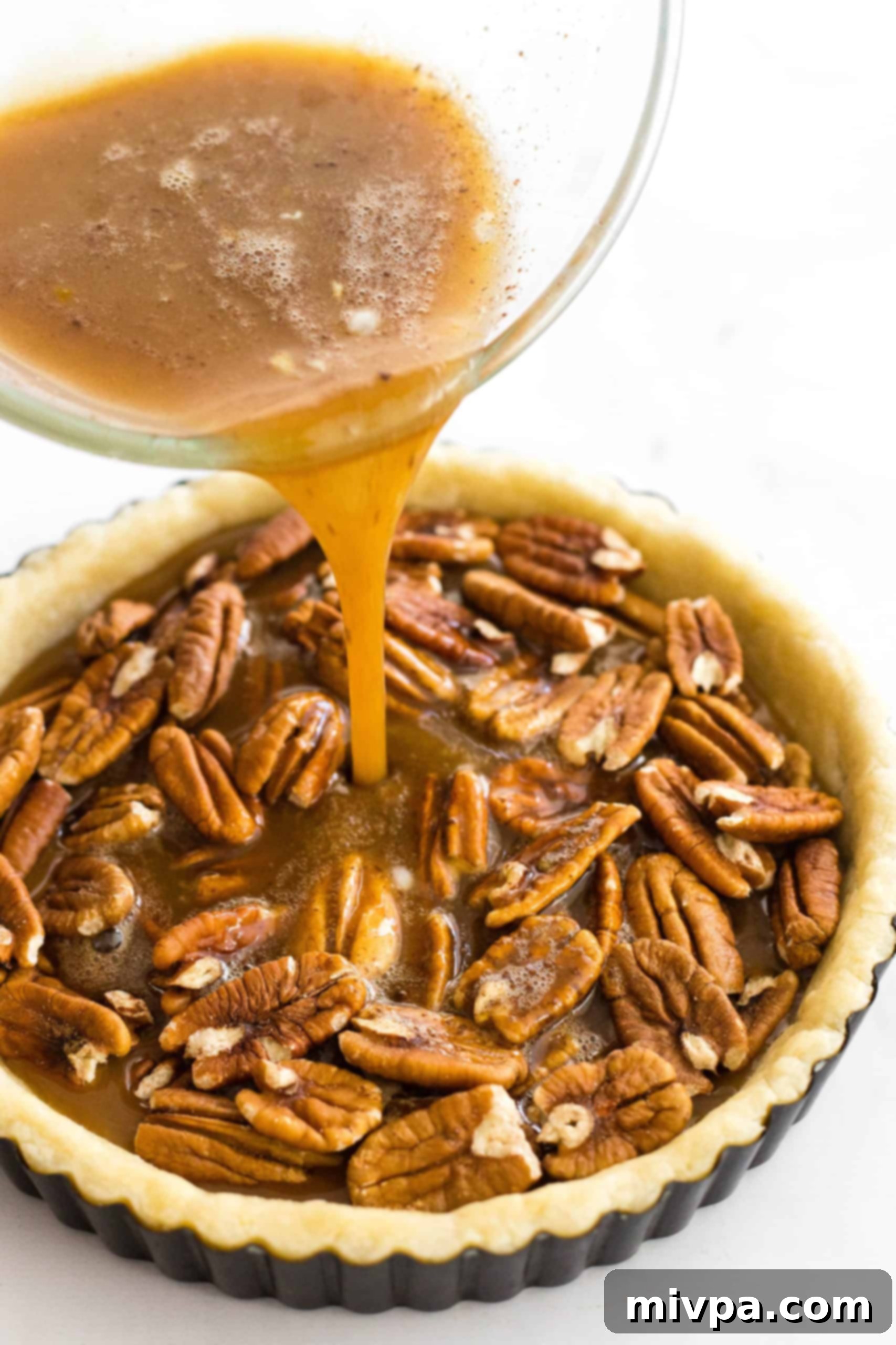 Easy Dairy-Free Pecan Pie (Gluten-Free) Pouring brown liquid into a crust filled with pecan nuts.