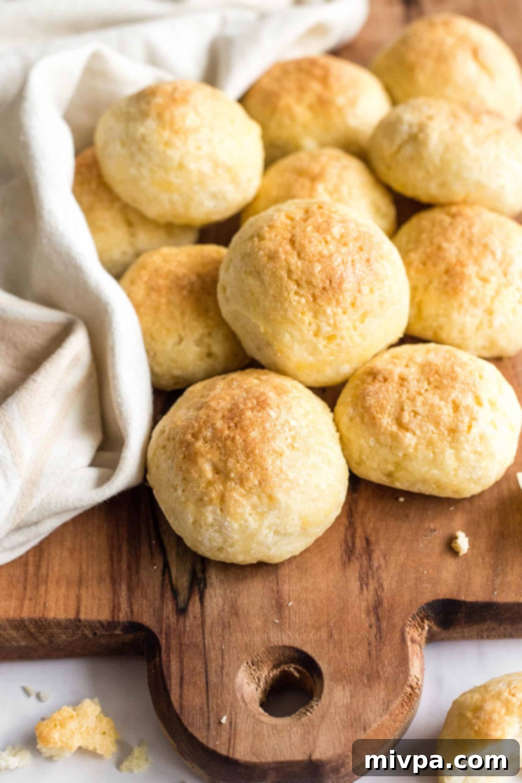 Piles of soft, golden brown gluten-free dinner rolls on a rustic wooden board, ready to be served.