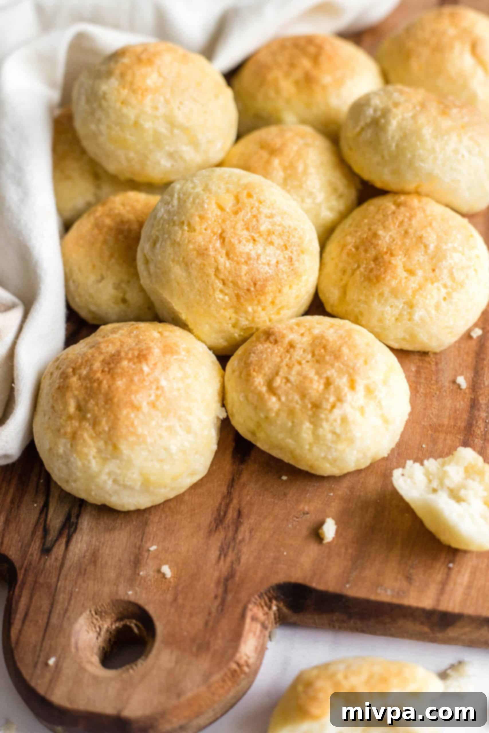 A large pile of soft, golden-brown gluten-free dinner rolls on a wooden board, ready for serving.