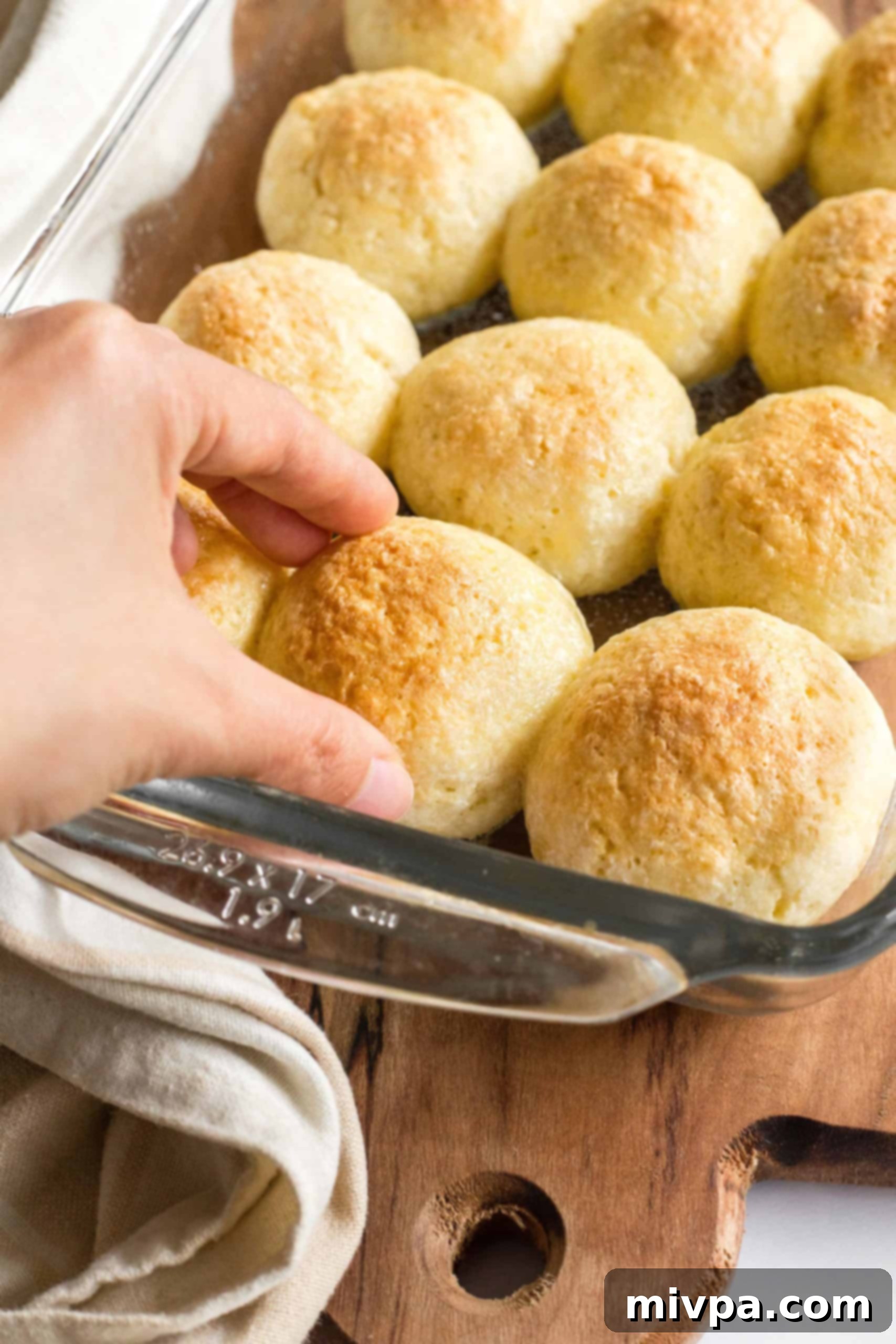A hand gently reaching for a warm, freshly baked gluten-free bread roll from a glass baking pan.
