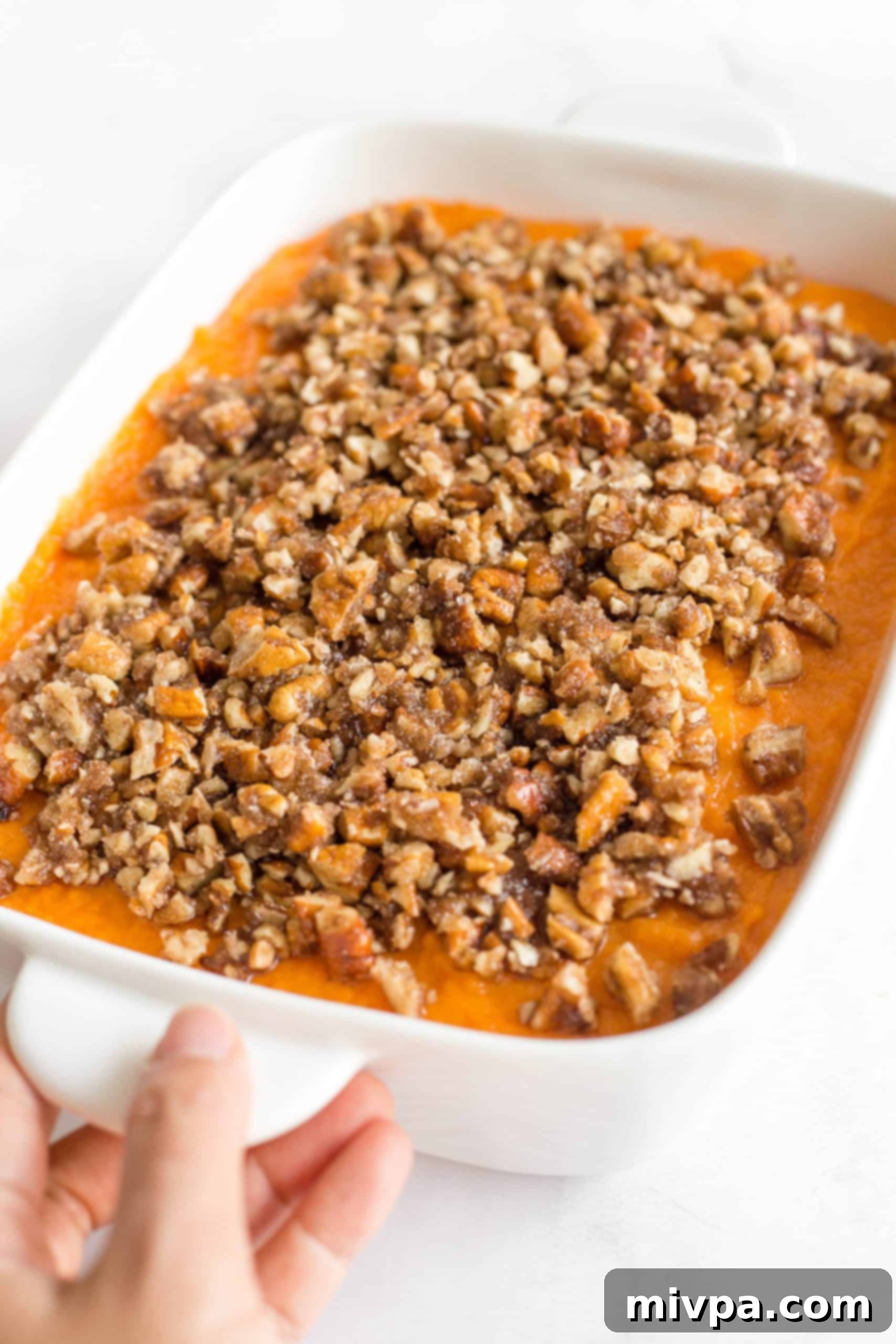 Easy Sweet Potato Casserole (Gluten-Free, Dairy-Free) Hand holding a casserole dish with sweet potato casserole.