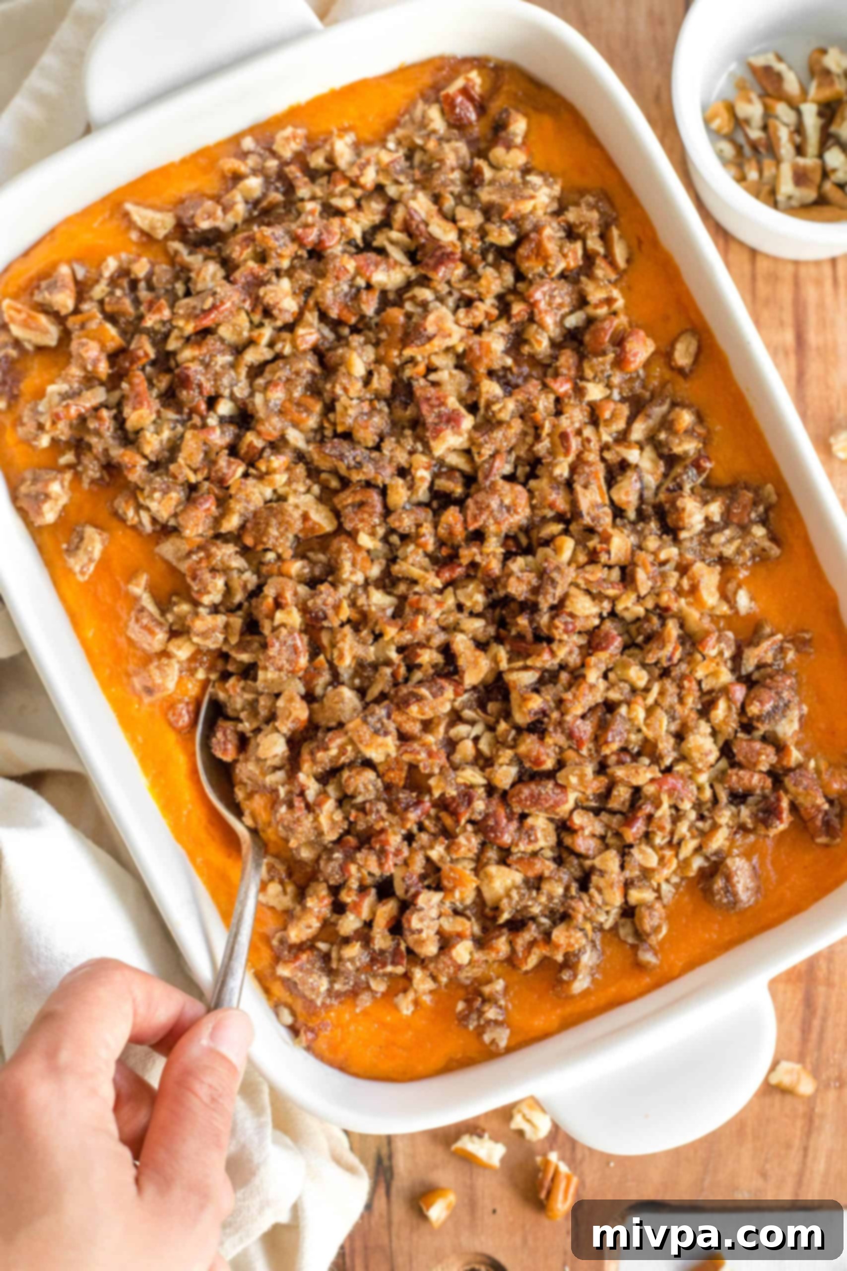 Sweet Potato Casserole (Gluten-Free, Dairy-Free) Hand holding a spoon in the casserole dish.