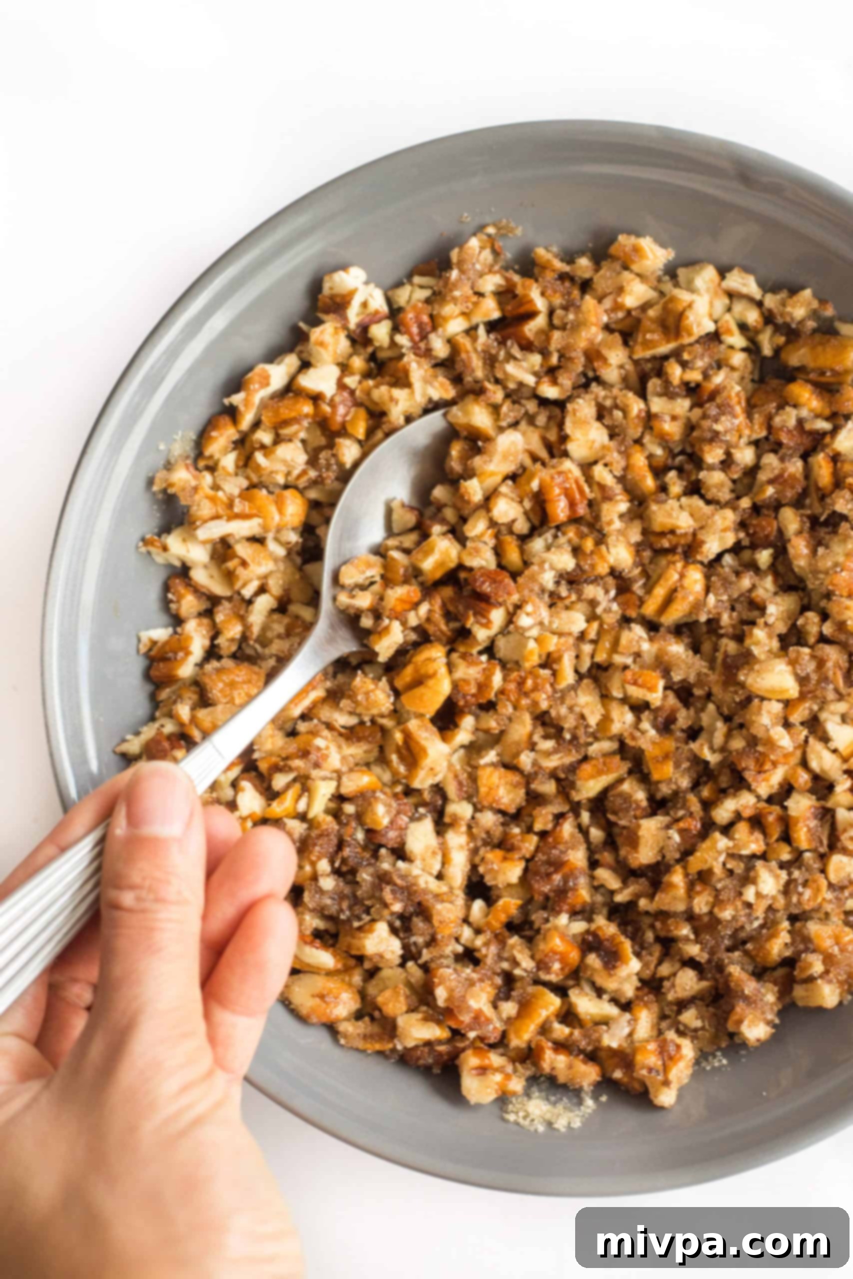 Gluten Dairy-Free Sweet Potato Casserole Hand mixing chopped pecans in a grey bowl.