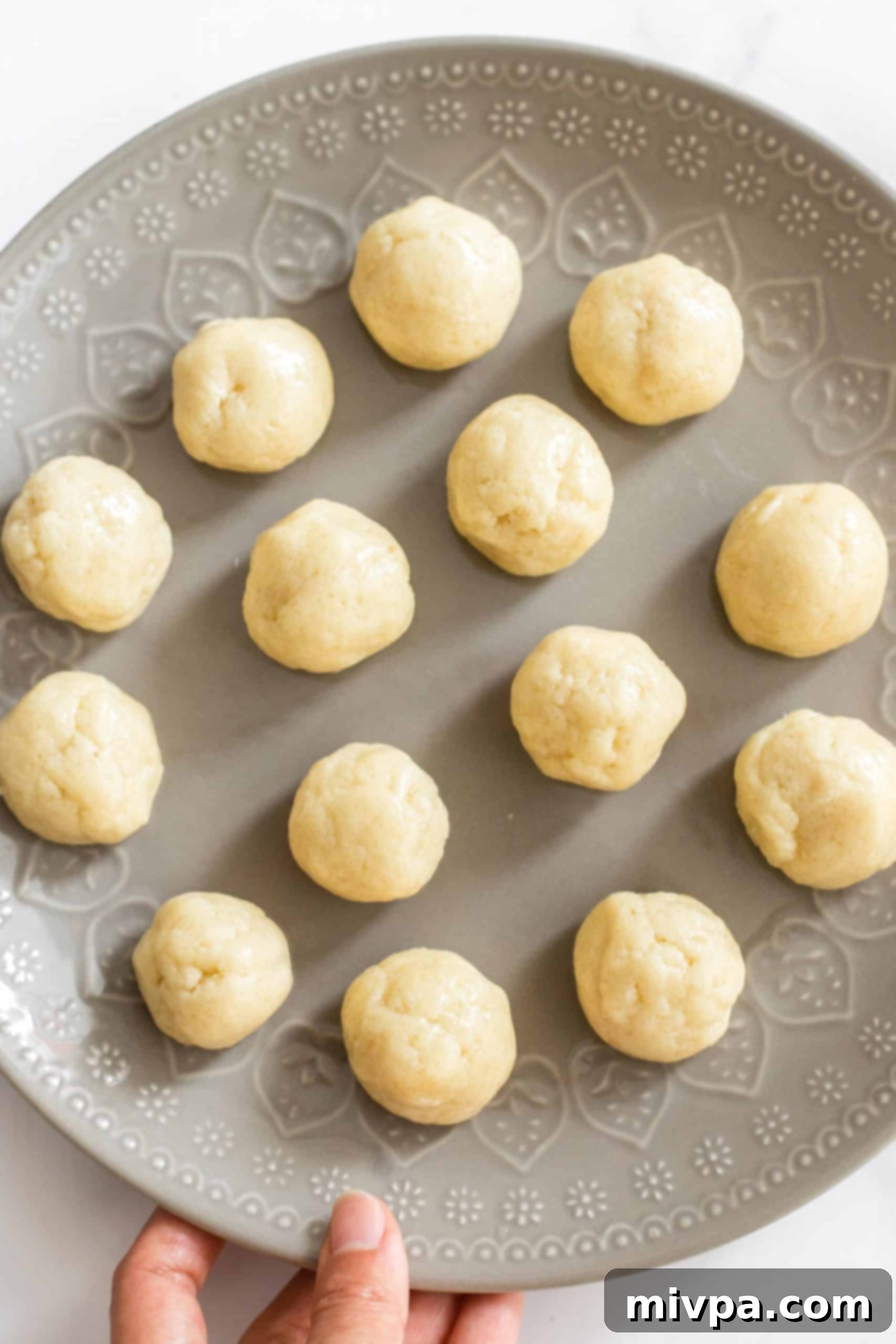 Perfectly rounded snickerdoodle cookie dough balls, ready for coating, arranged on a white plate.
