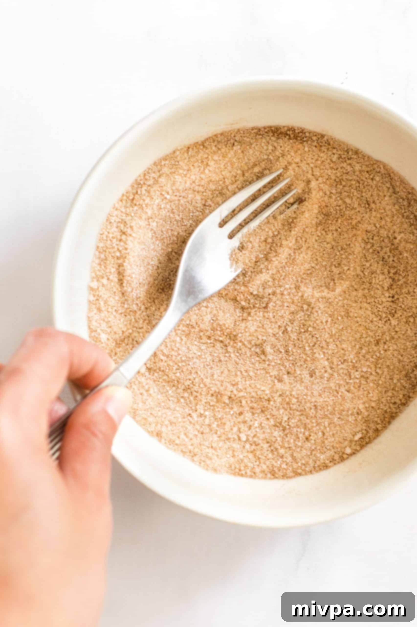 A fork mixing light brown sugar and ground cinnamon in a small white bowl to create the signature snickerdoodle coating.