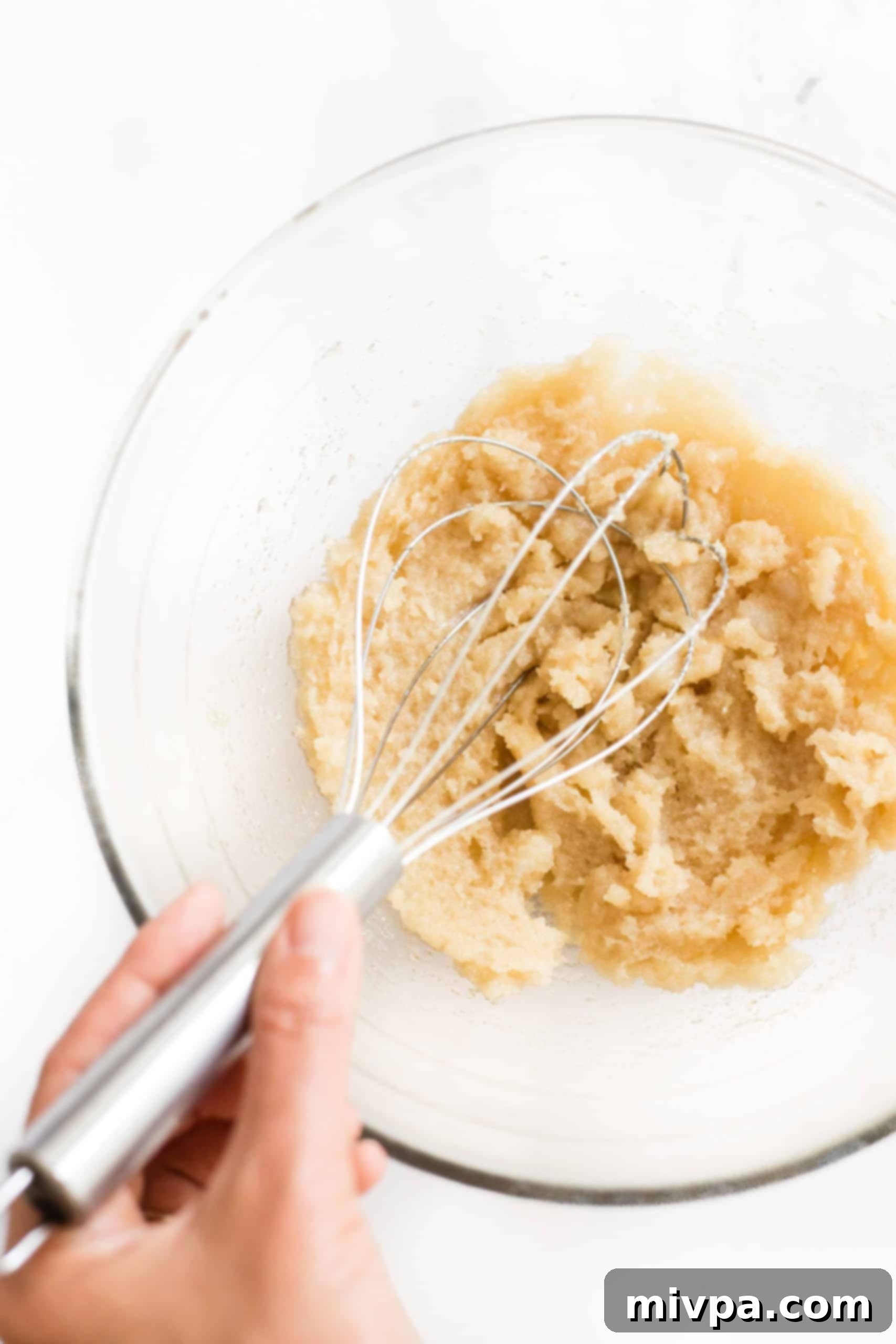 A close-up shot of light brown sugar and softened coconut oil being creamed together in a mixing bowl with a whisk.