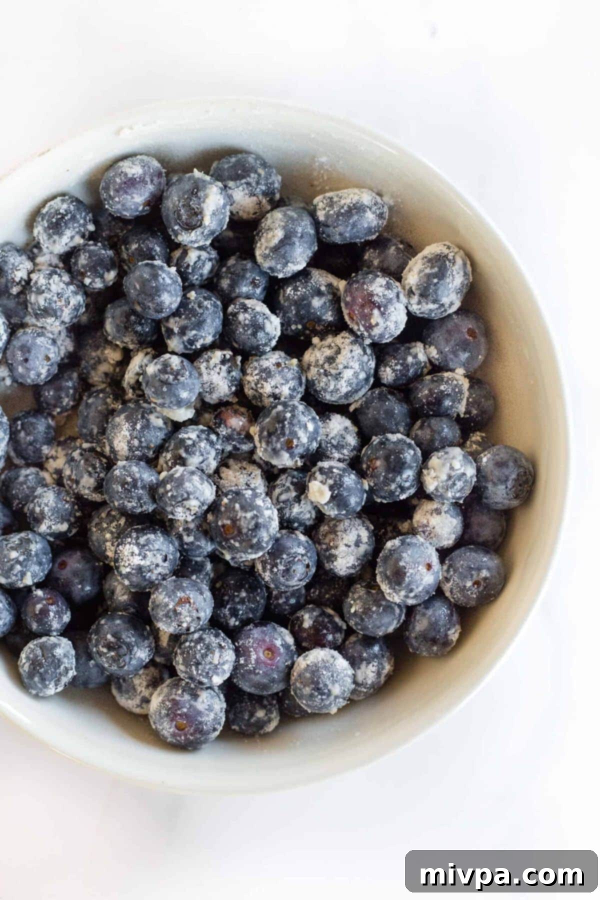 Flour-coated blueberries in white bowl.