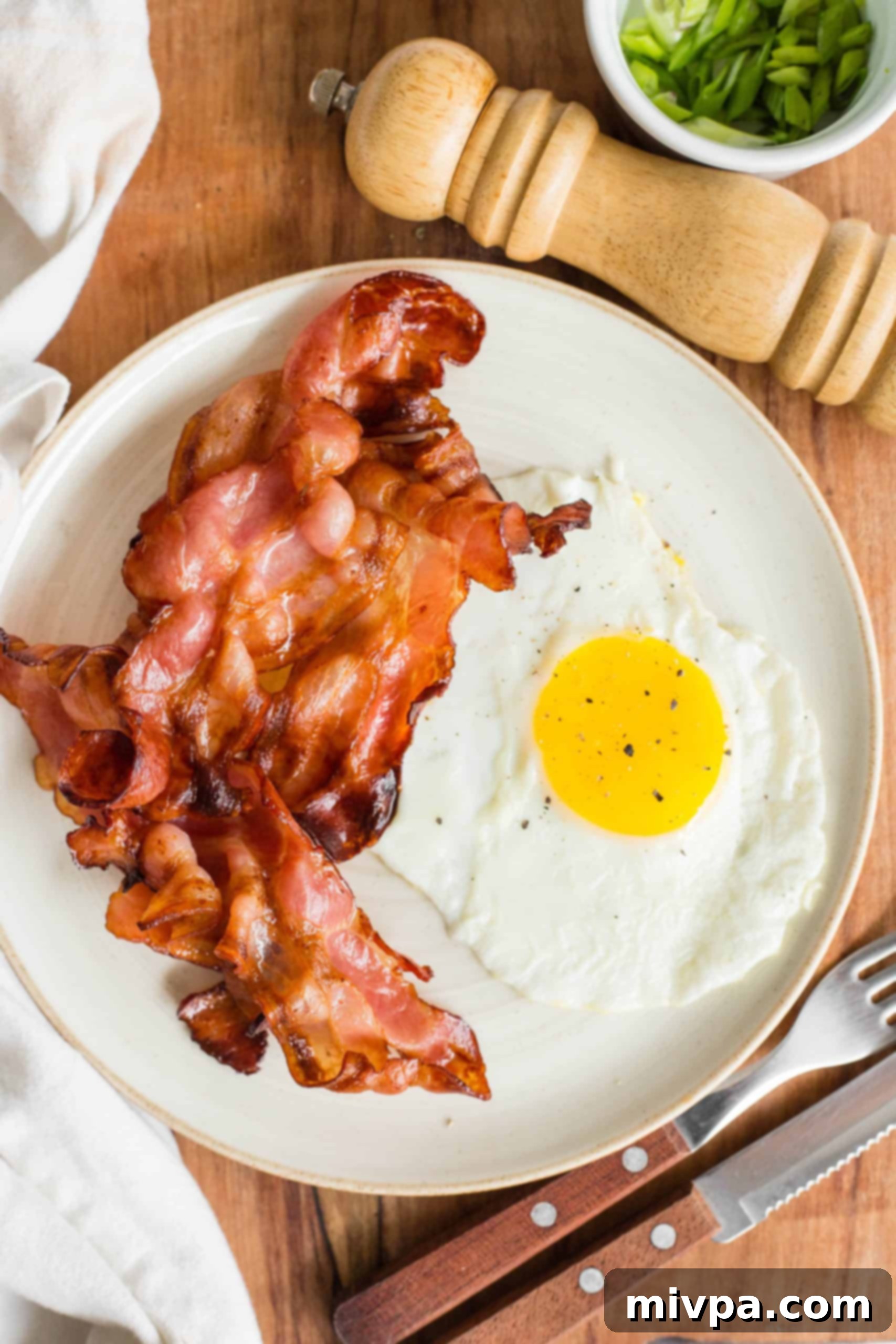Golden brown, crispy bacon slices served alongside a perfectly fried egg on a white plate, ready to be enjoyed.