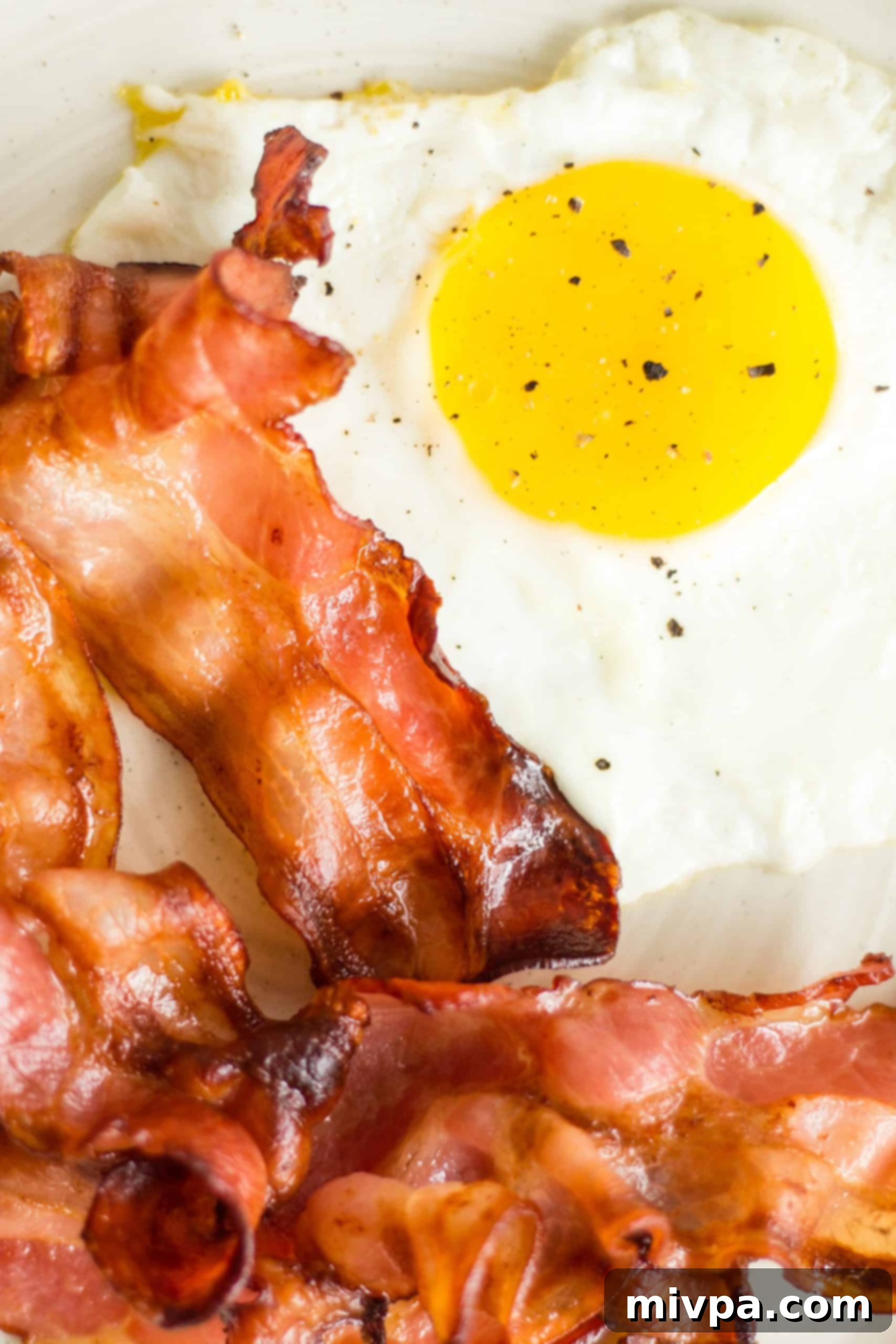 A vibrant close-up shot of crispy bacon slices and a sunny-side-up egg, garnished with fresh herbs.