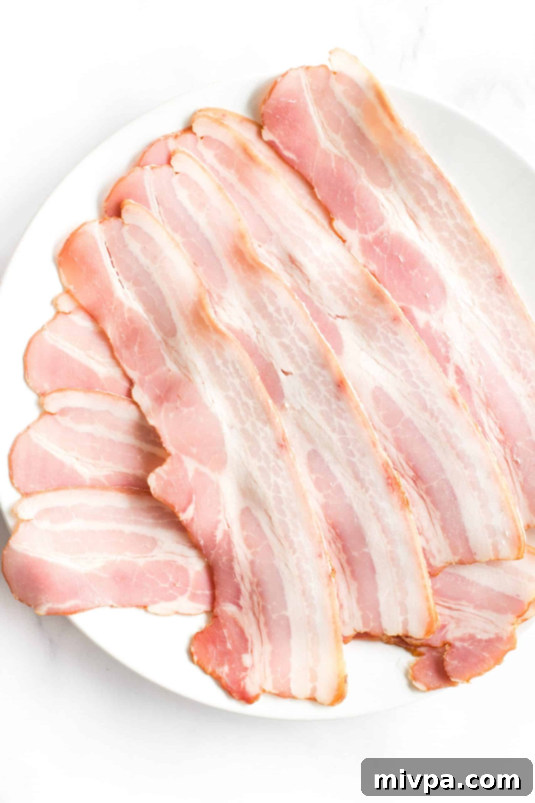 Uncooked bacon slices, neatly arranged on a white plate, ready for the air fryer.