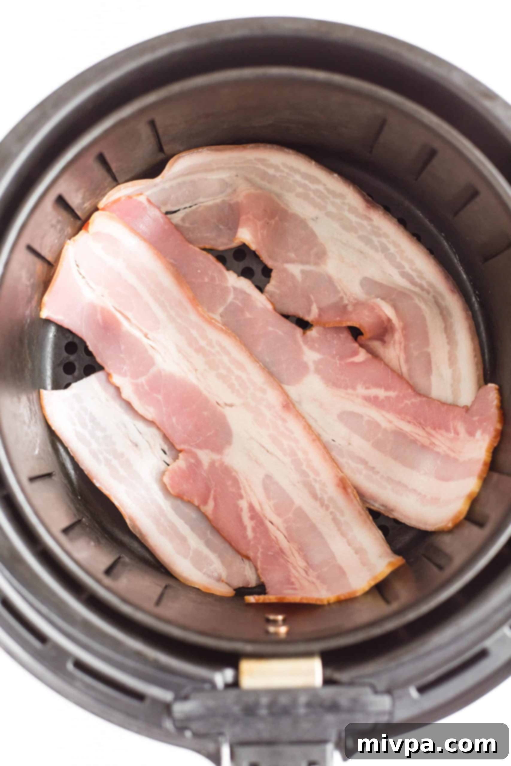 Uncooked bacon slices perfectly arranged in a single layer inside an air fryer basket.