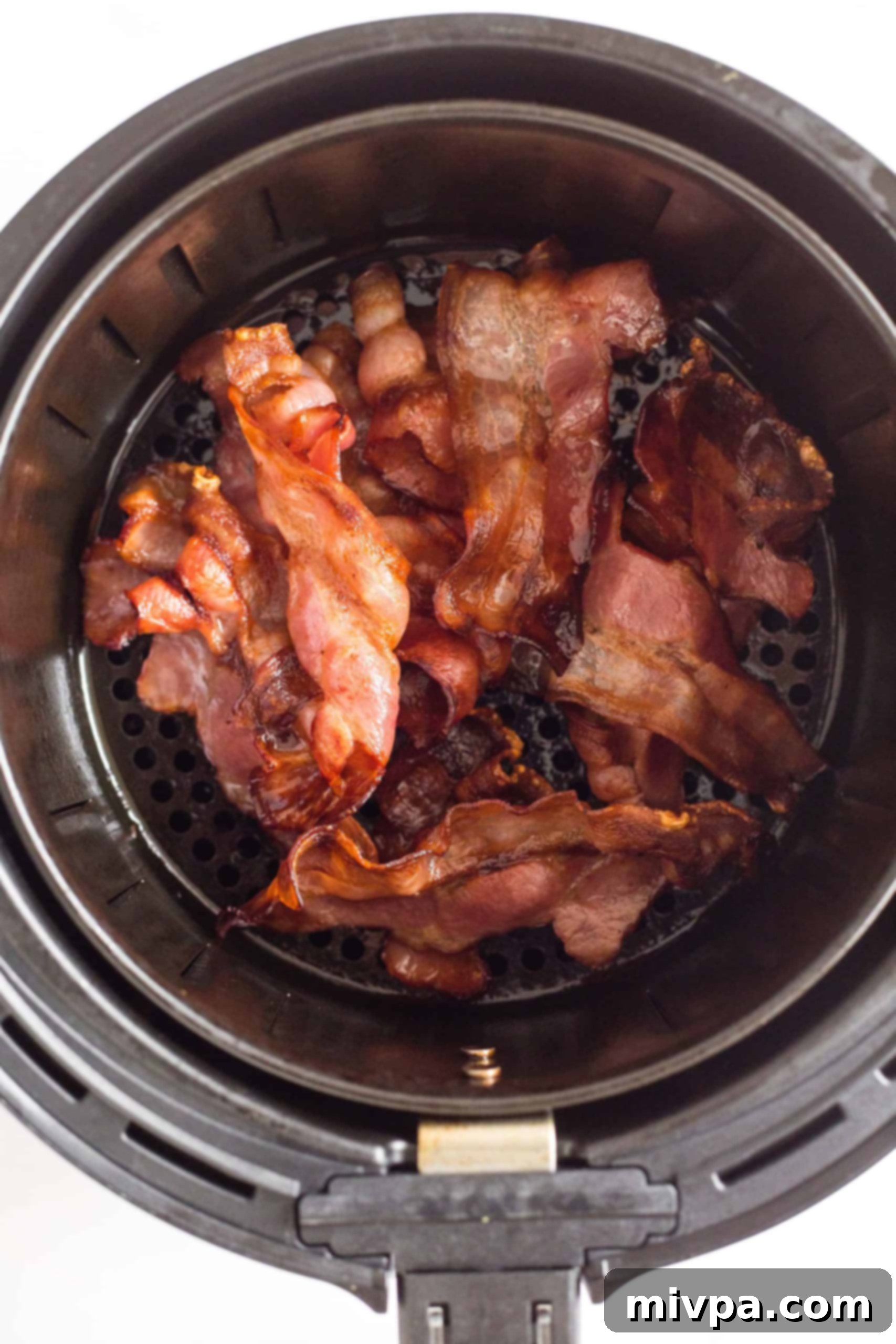 Freshly cooked air fryer bacon arranged in an air fryer basket, ready for serving or a quick reheat.