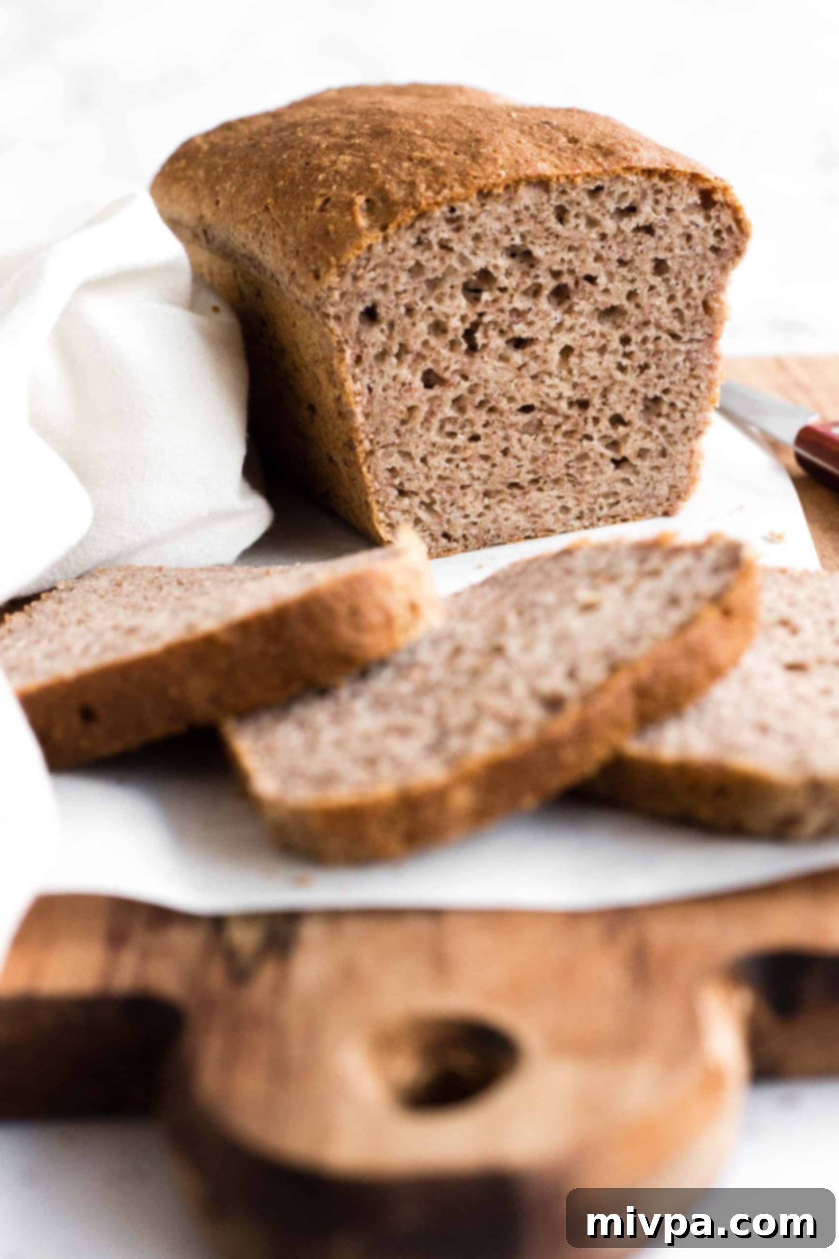 Sliced loaf of buckwheat bread on parchment-lined board.