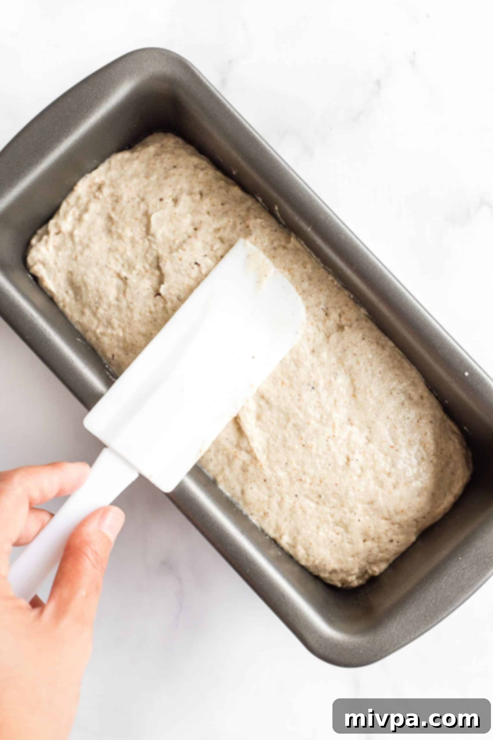 Smoothing out the top of the bread dough in a loaf pan with a spatula.