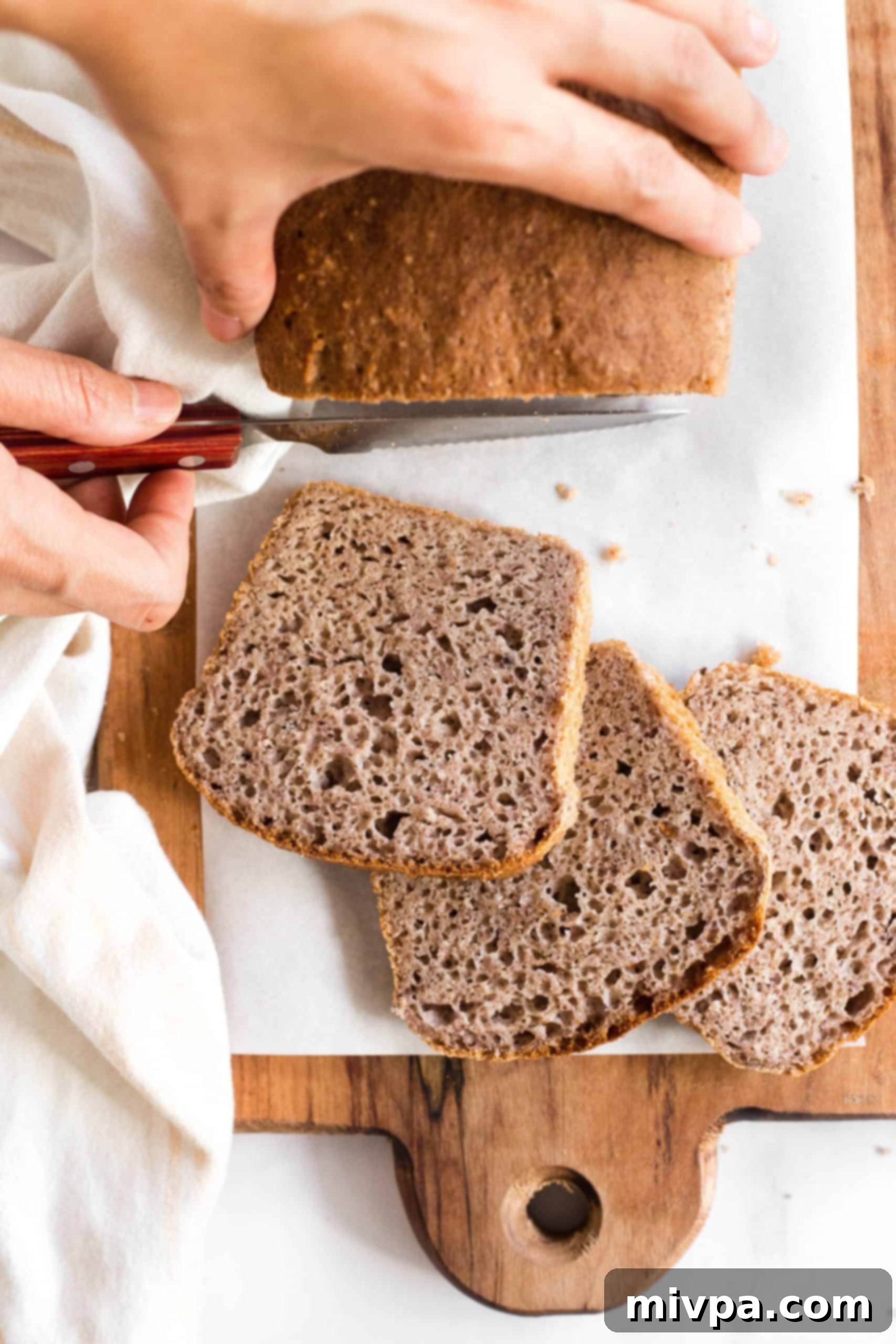 Hand slicing into a loaf of bread on a wooden board.