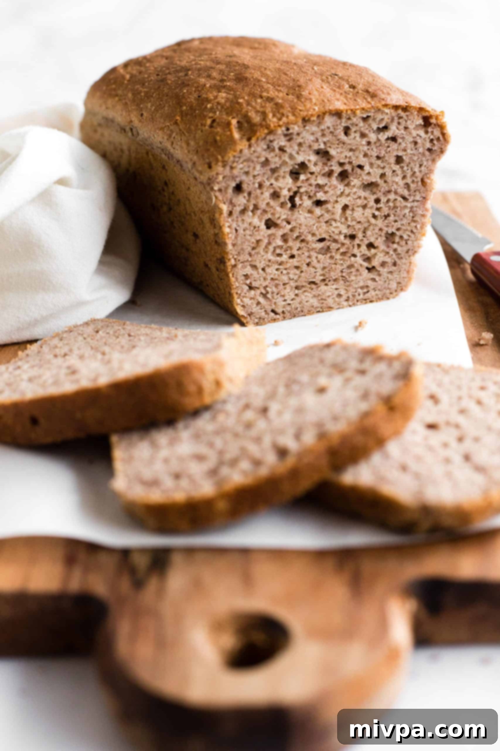 A half-sliced loaf of bread on parchment-lined wooden board.
