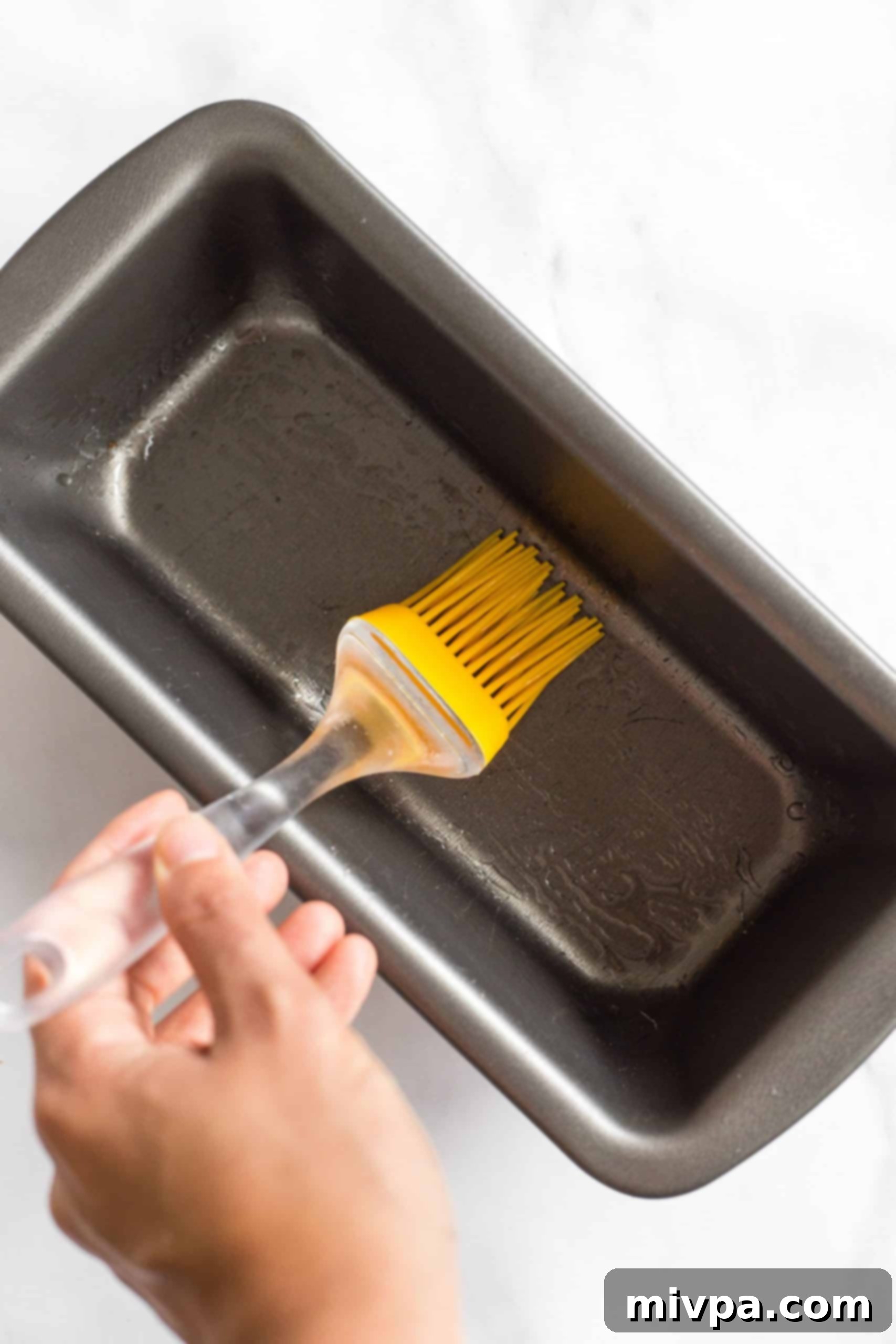 Brushing a metal loaf pan with oil.