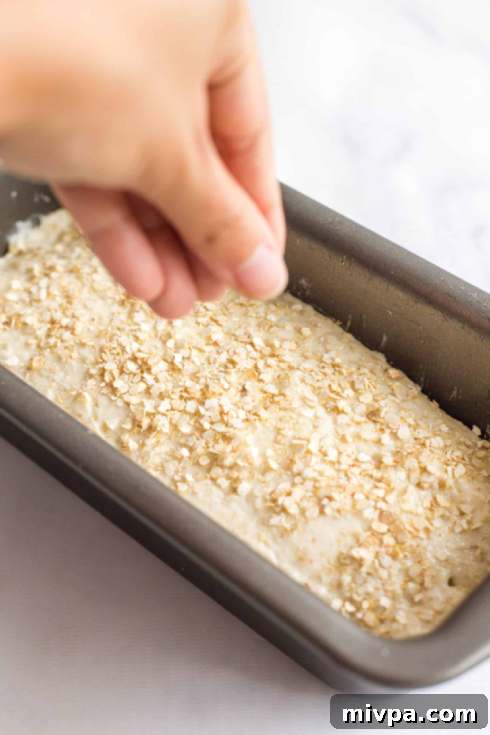 Sprinkling quinoa flakes over batter in a metal loaf pan.