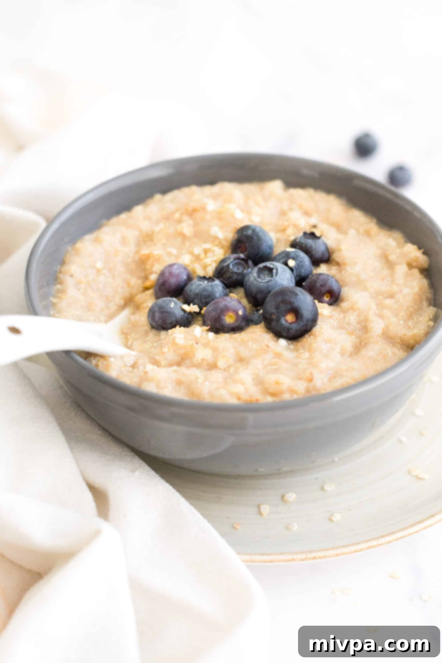 A spoon dipping into a bowl of creamy quinoa porridge topped with vibrant blueberries, highlighting its inviting texture.